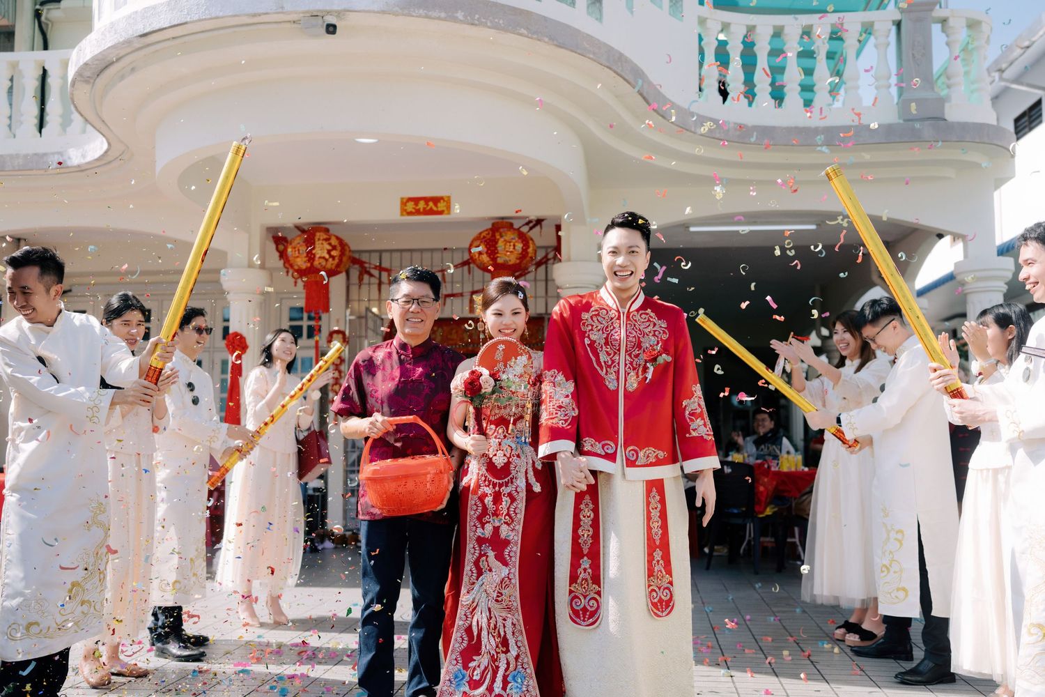 Couple celebrating traditional Chinese wedding door games with gold confetti cannons and red Qun Kwa bridal embroidery