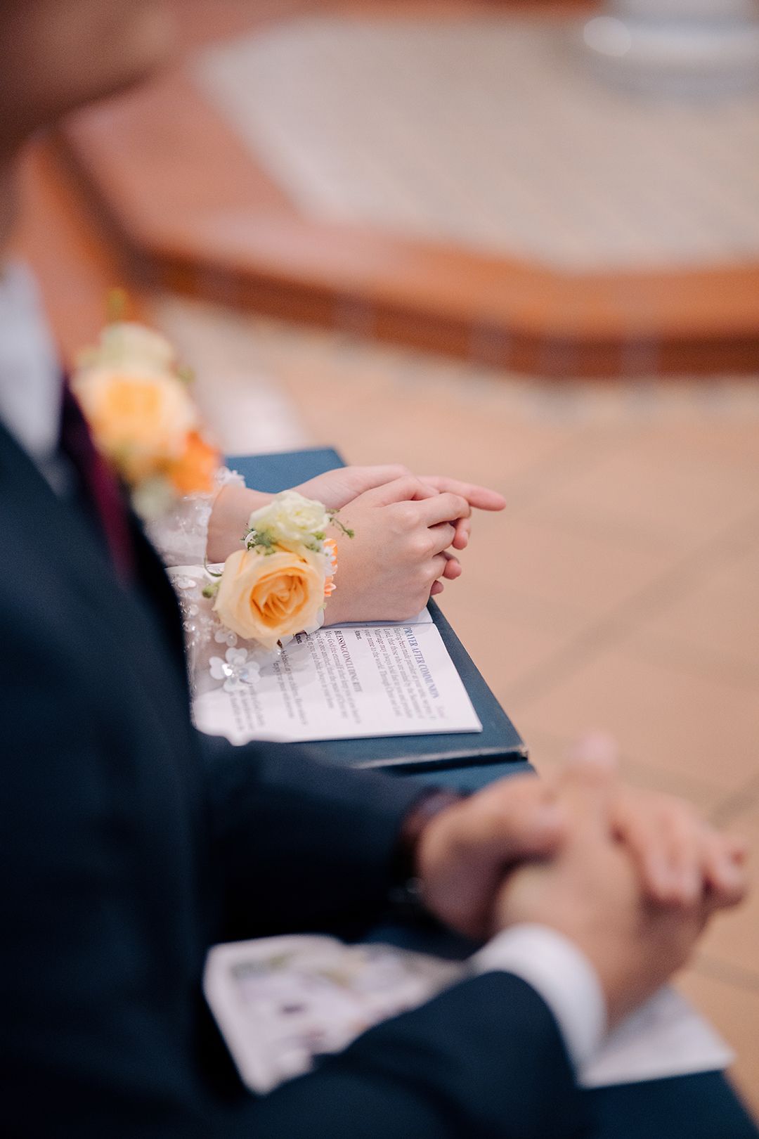 Close-up of a couple's hands with yellow rose corsages resting on a wedding program