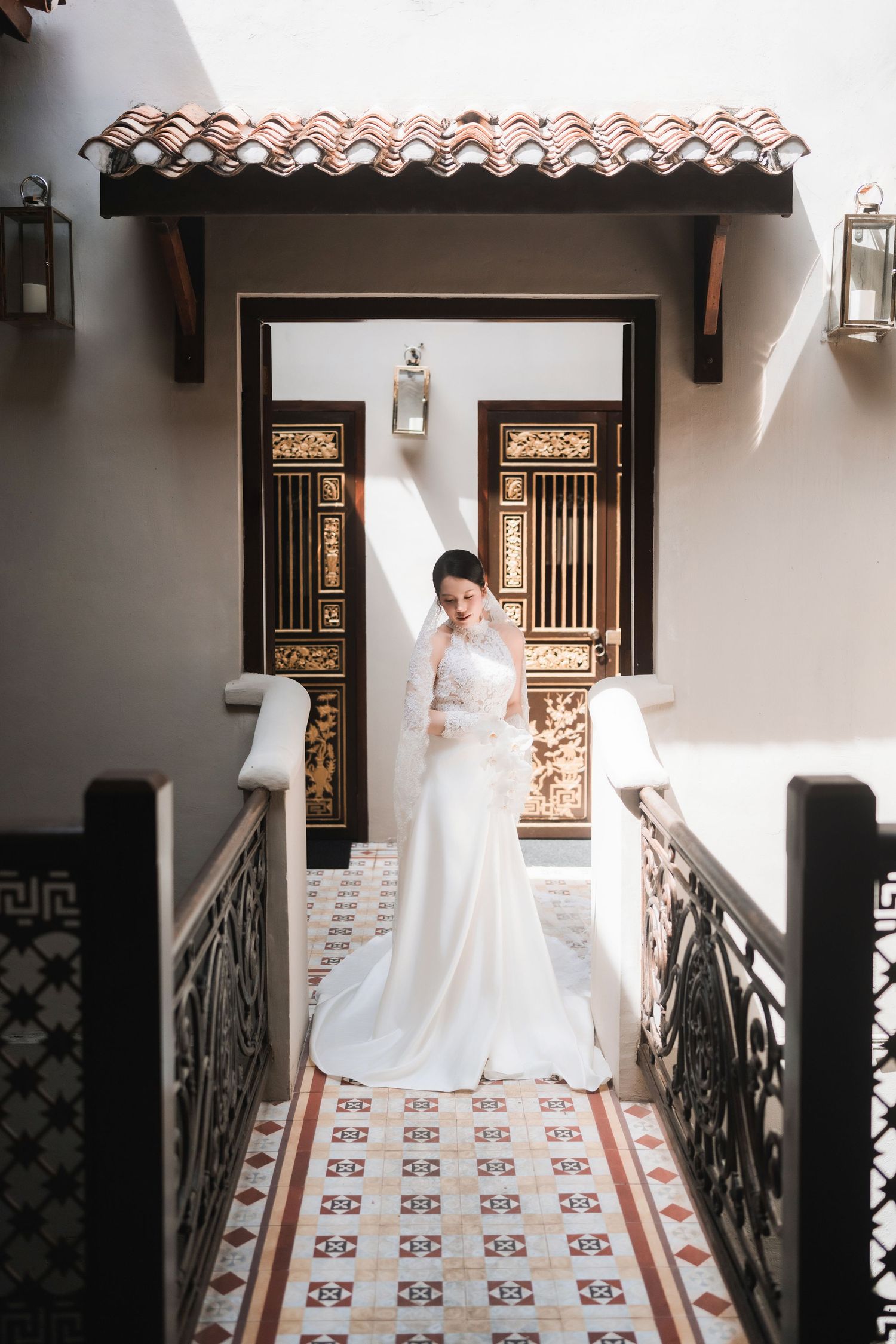 Bride in flowing white gown walking along tiled corridor with Spanish colonial architecture.