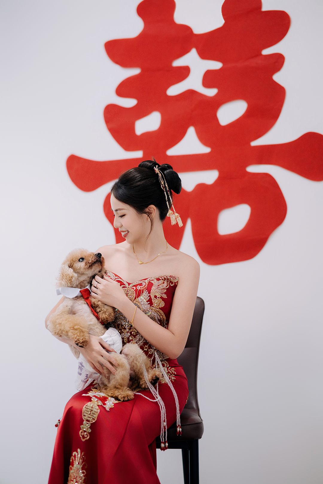 A person in a red dress holds and plays with a small dog against a white background with red symbols.