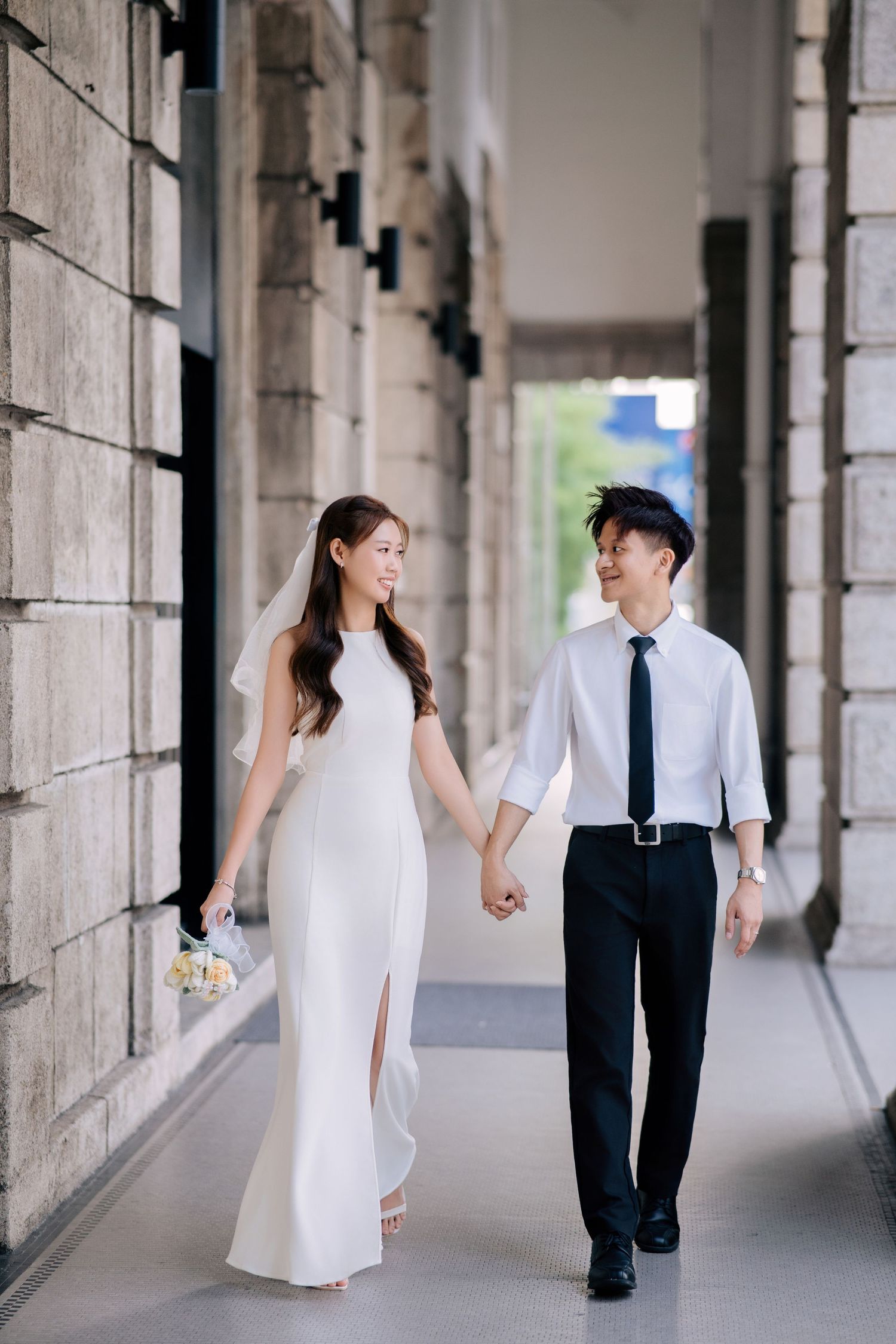 Couple in wedding attire walking through a colonnade hallway.