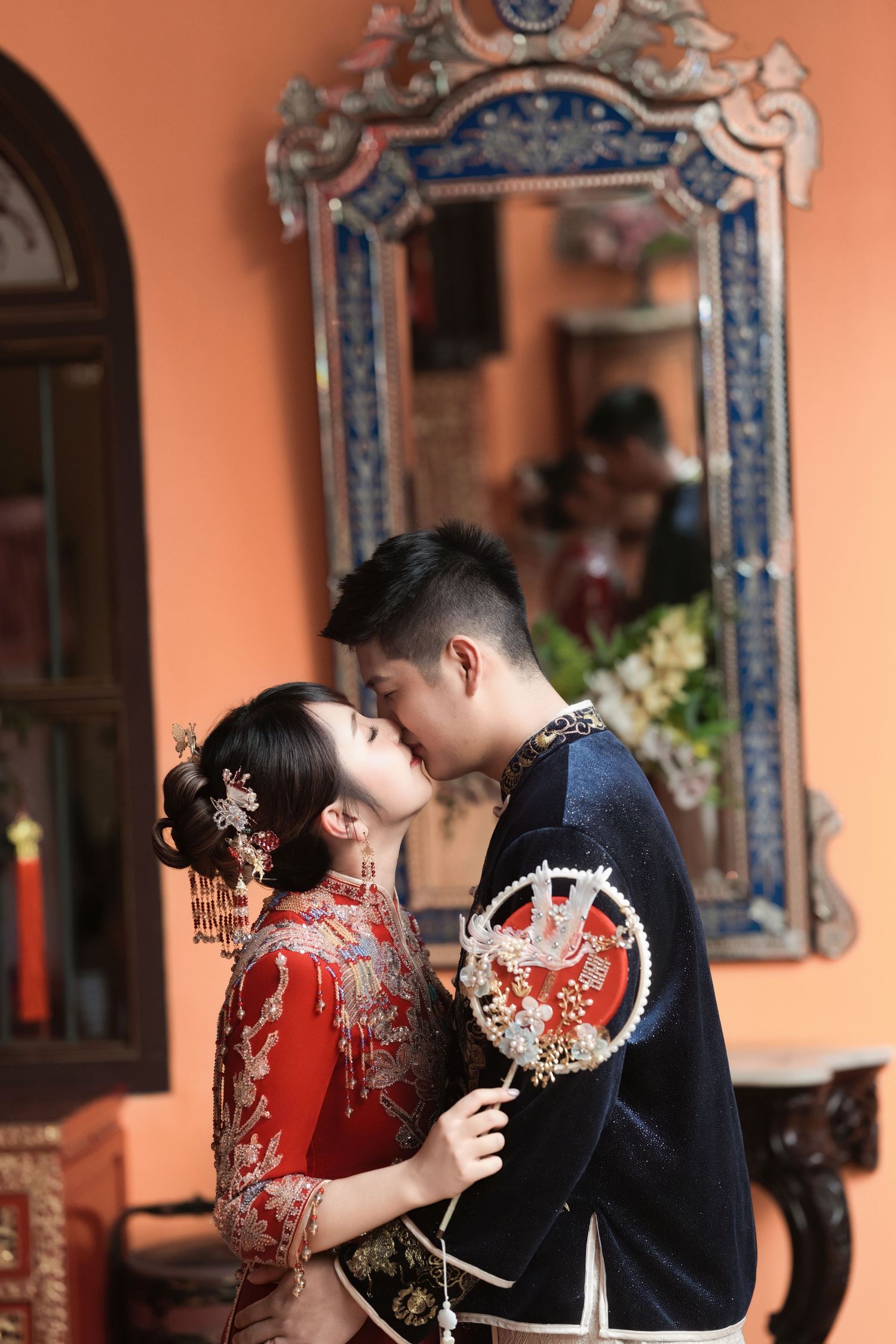 Traditional Chinese wedding couple share an intimate moment in an ornate hallway with decorative blue mirrors.