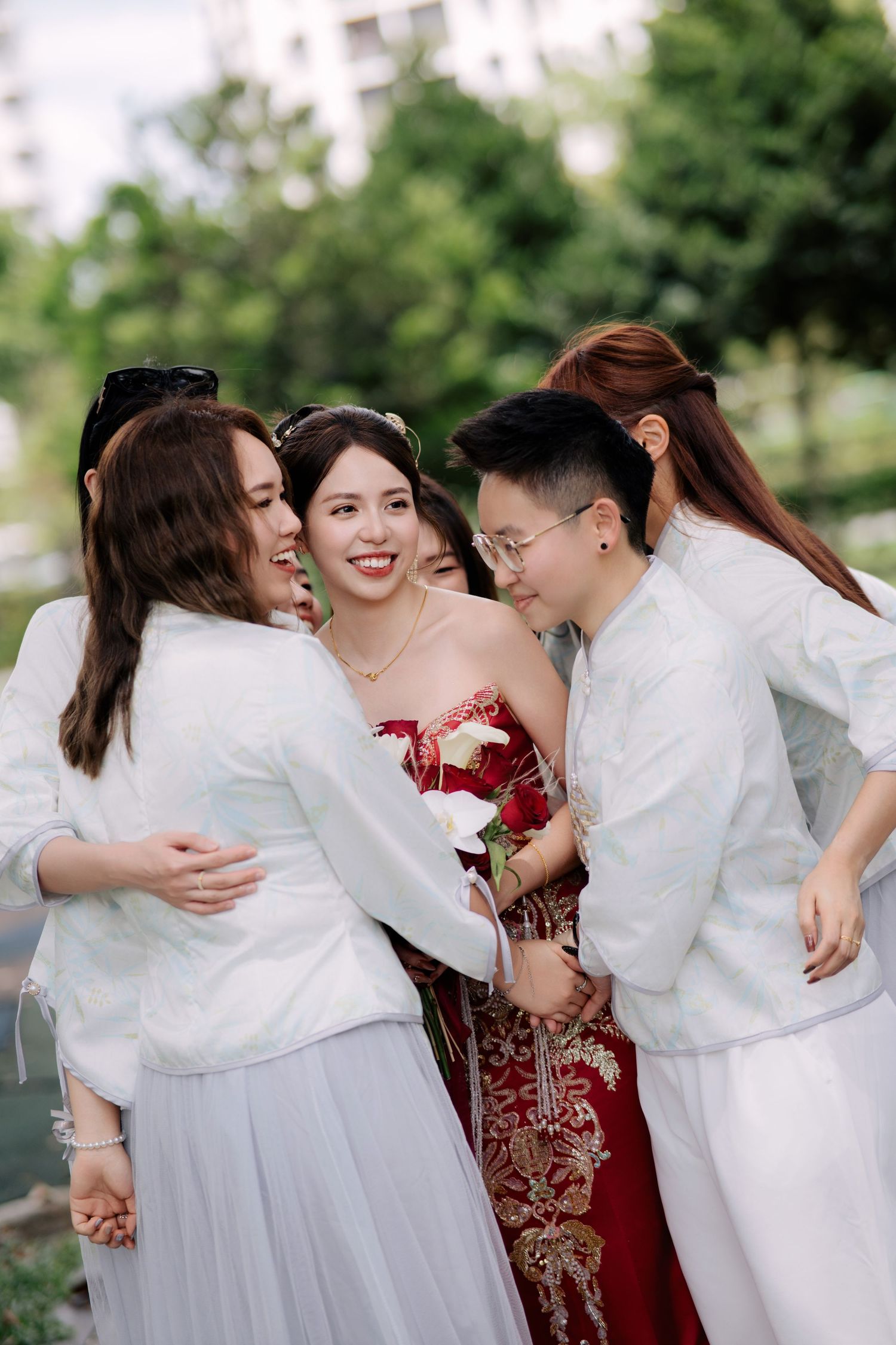Wedding party in white attire embracing and sharing joyful moments outdoors.