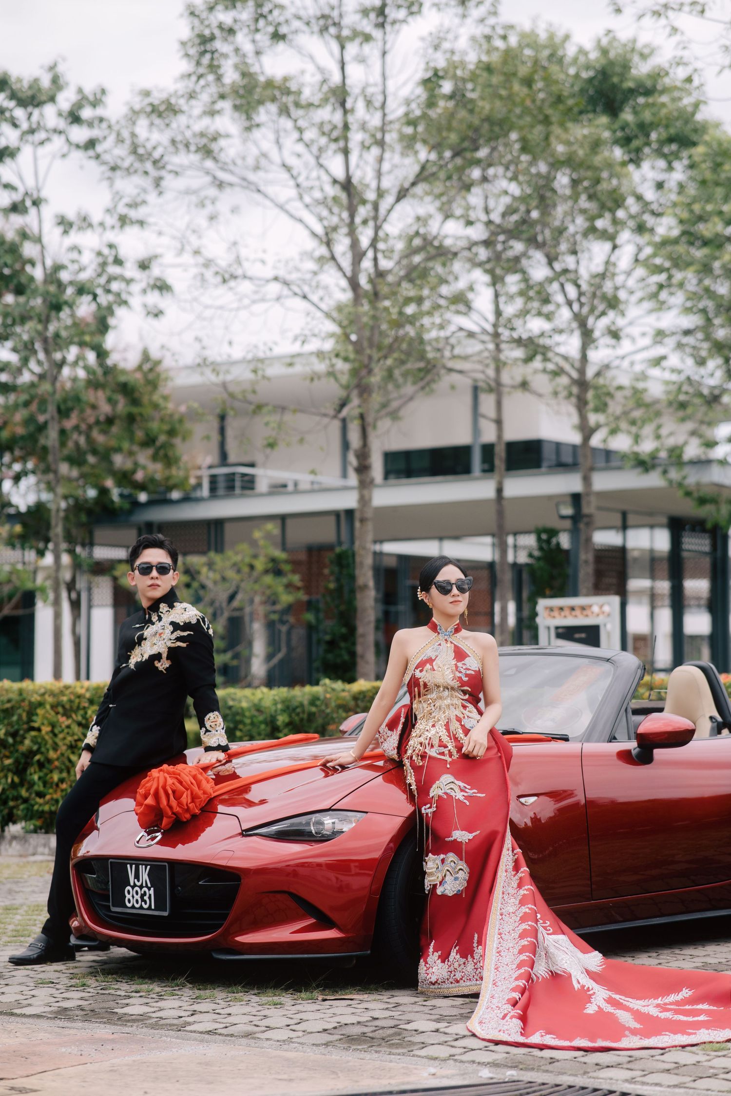 Modern Chinese wedding couple posing with a red luxury bridal car in traditional outfits