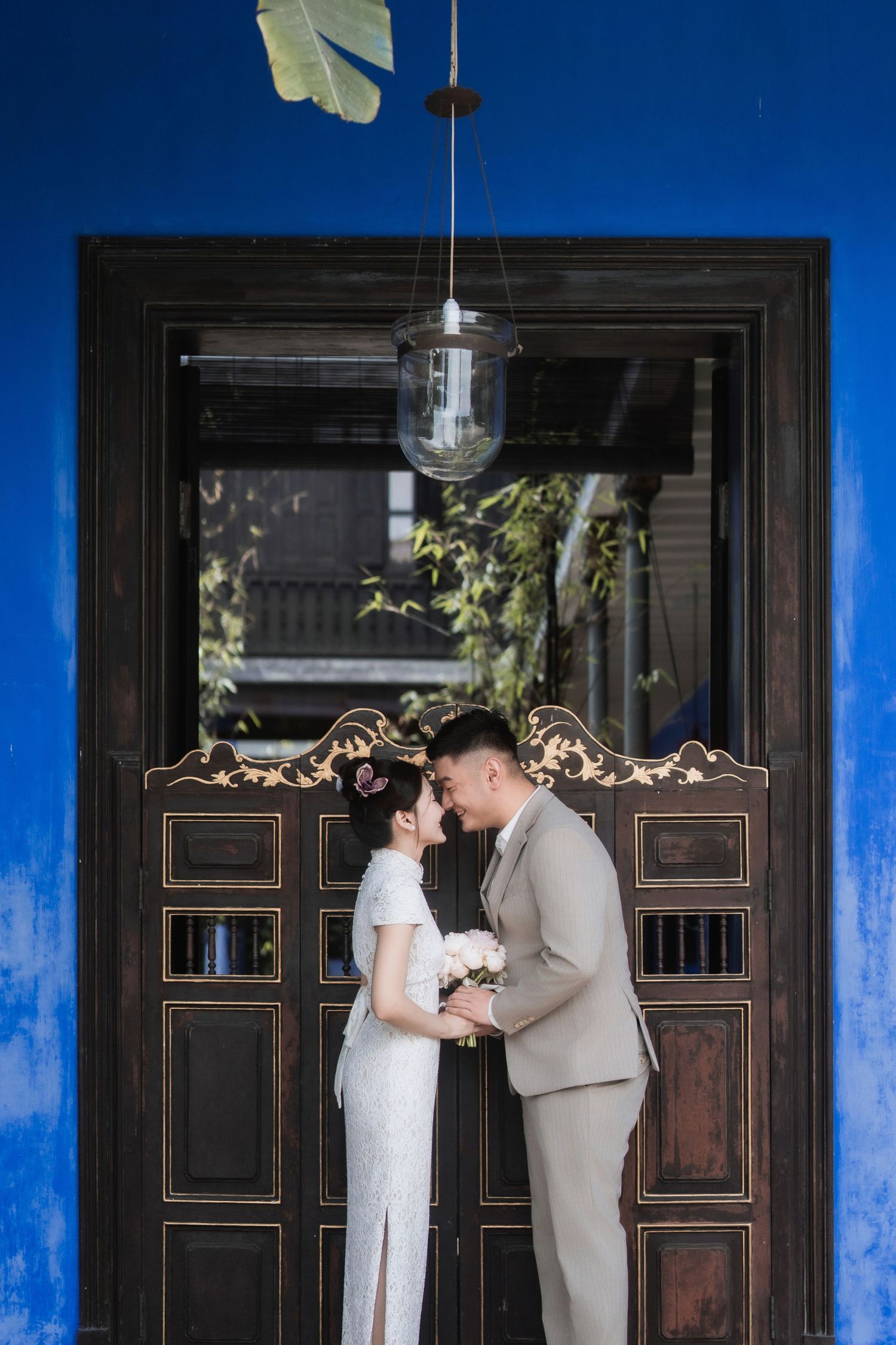 Couple posing behind the iconic swinging doors of Blue Mansion Penang against bright indigo walls
