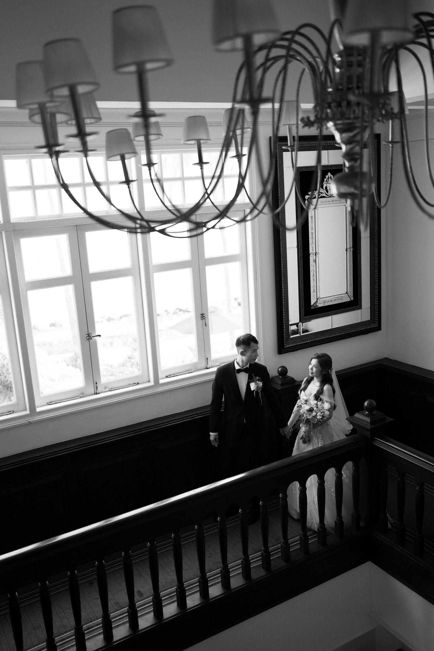 Couple holding hands on a wooden staircase, capturing the timeless feel of classic black and white wedding portraits at E&O Hotel