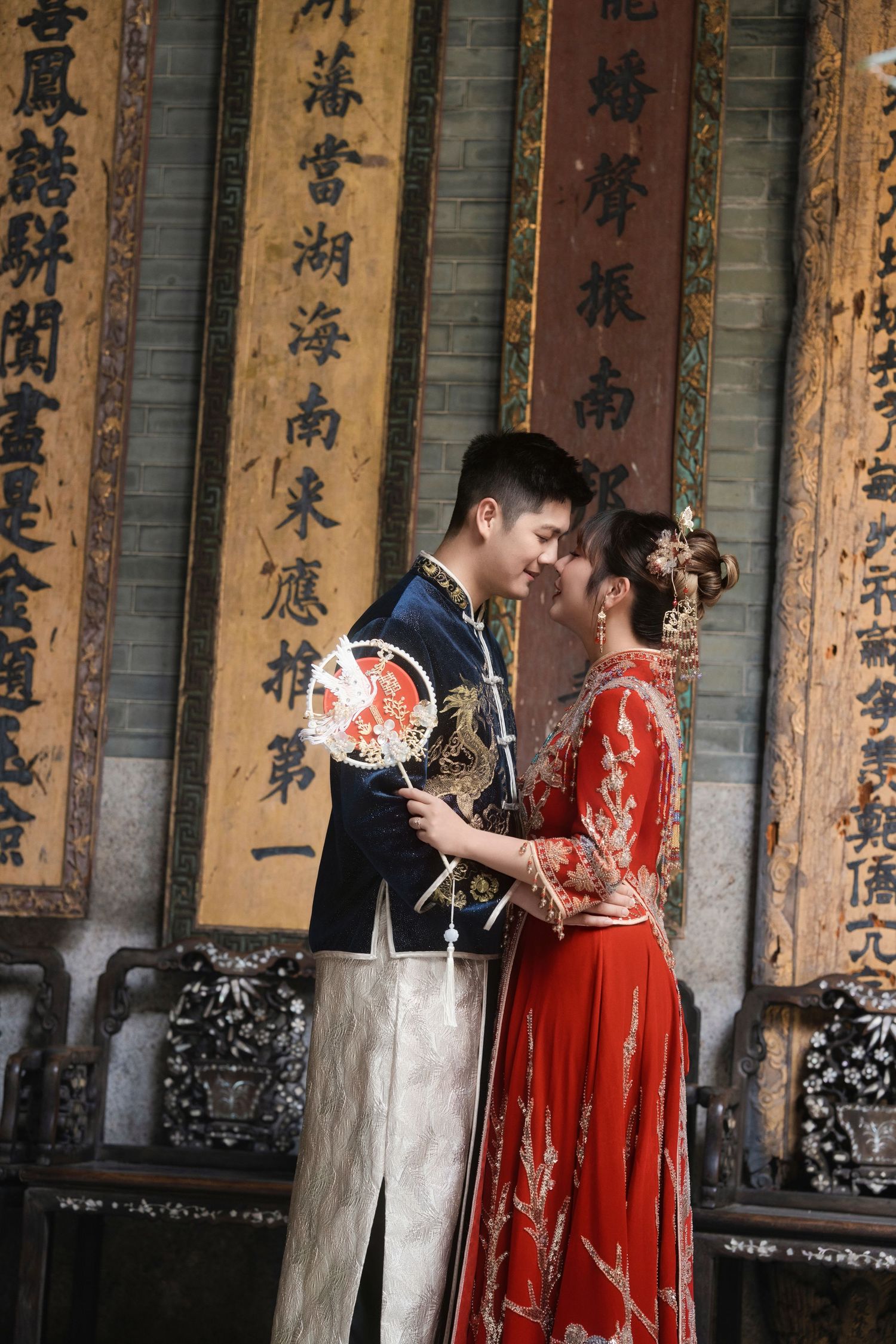 Intimate wedding photography of a couple in traditional Chinese wedding attire with a phoenix fan