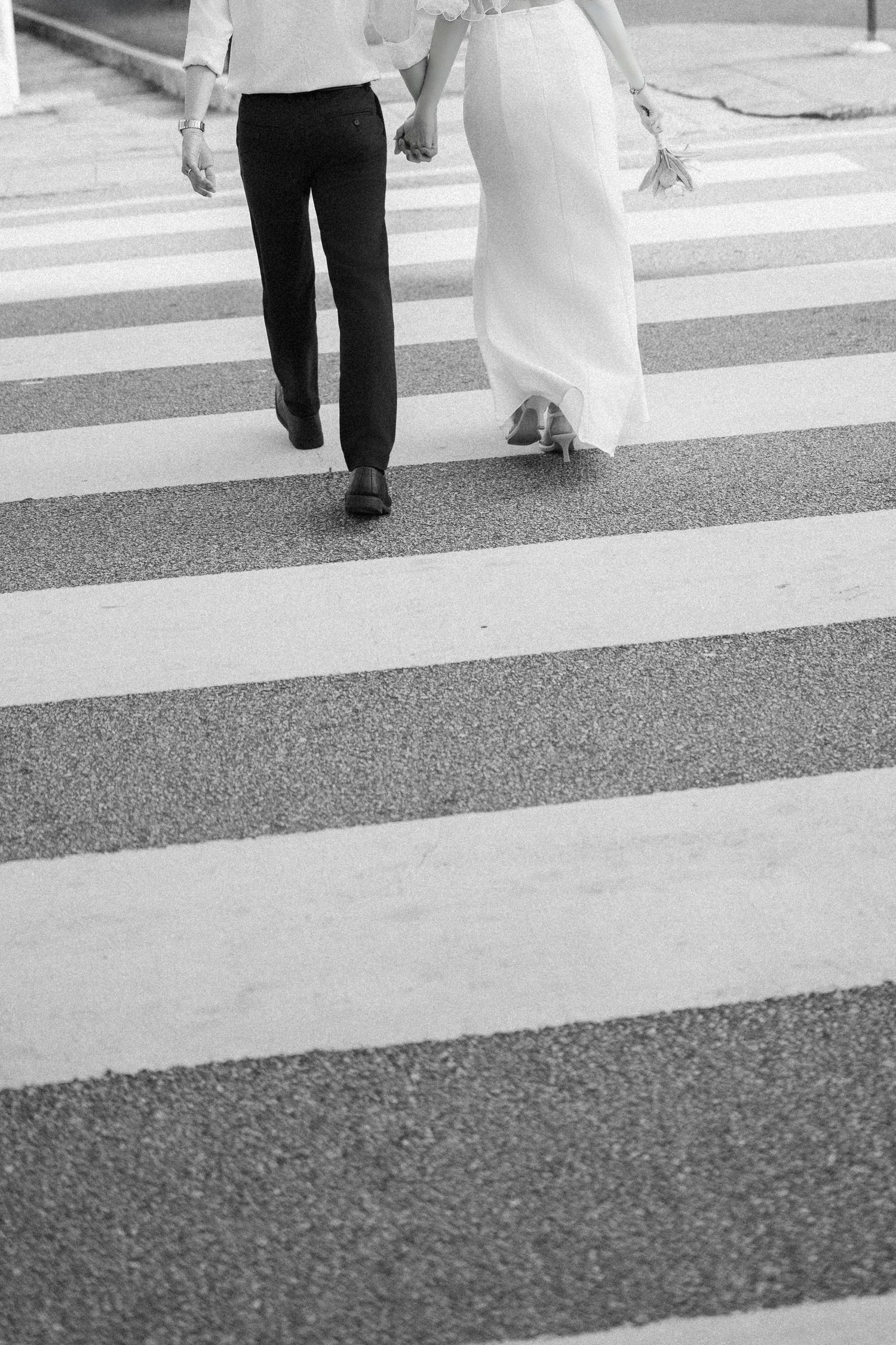 Black and white image of couple crossing street in wedding attire.