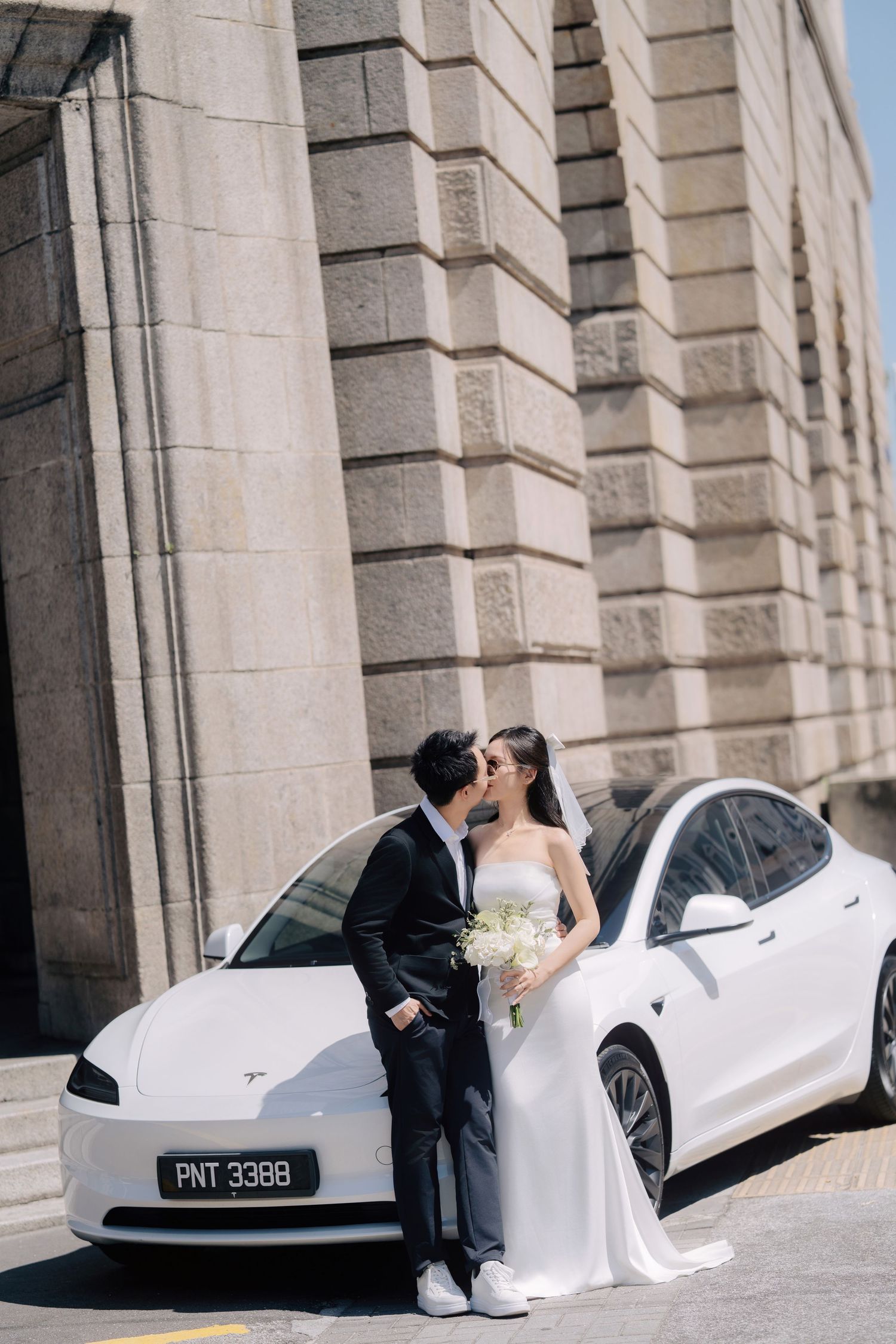 Wedding photo series with couple posing next to a white luxury car against stone columns.
