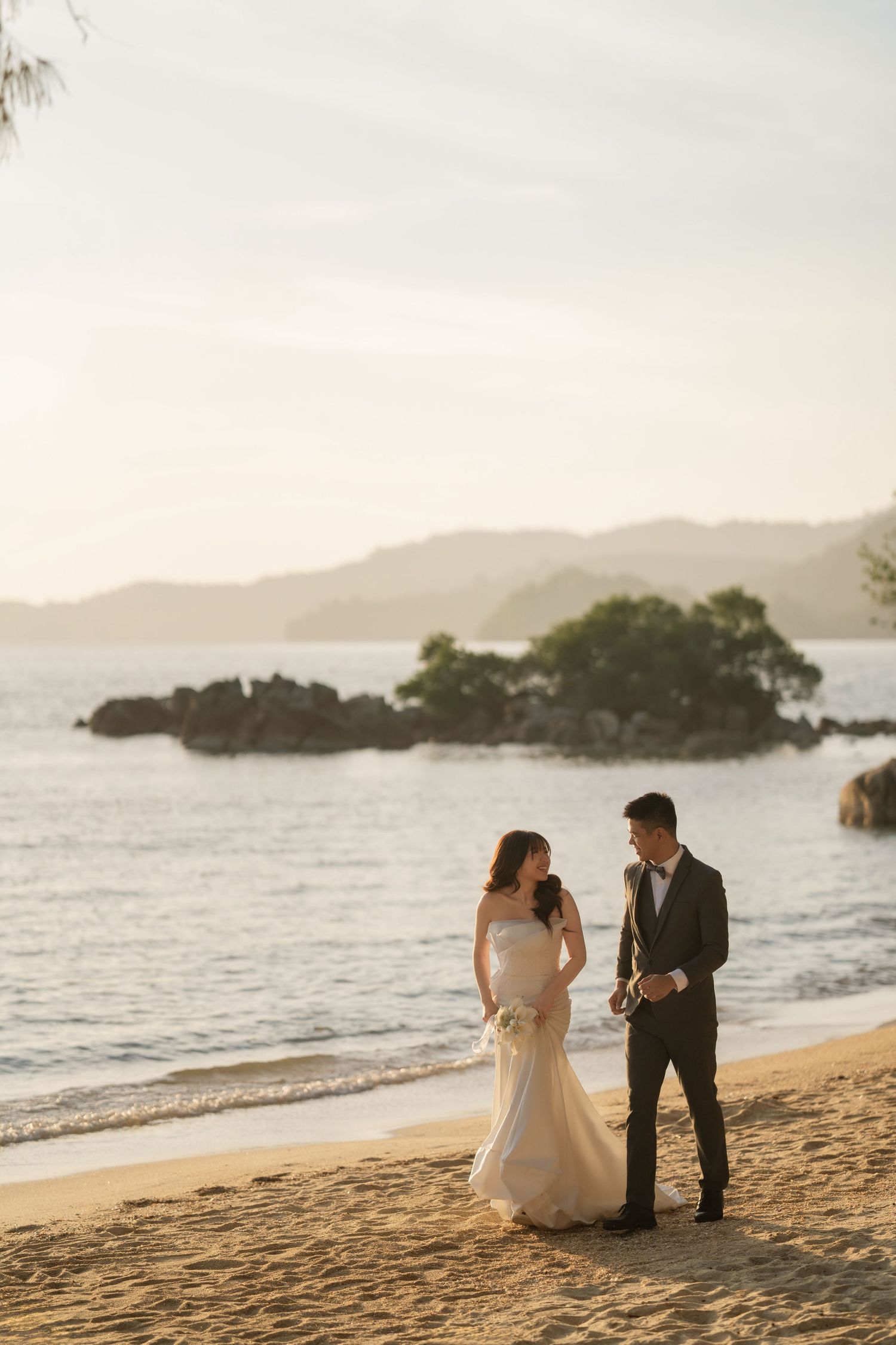 Wedding couple walking along a sandy beach with mountains in the distance.