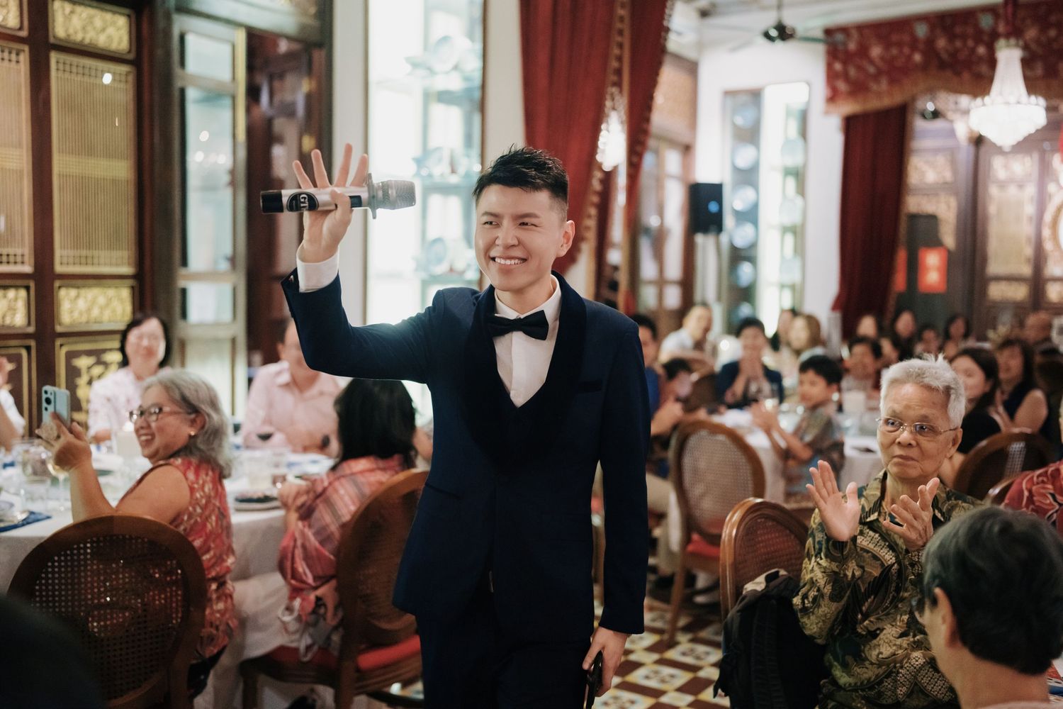 Groom holding a microphone and smiling at guests during a first march in at traditional Kebaya Dining Room Penang wedding dinner
