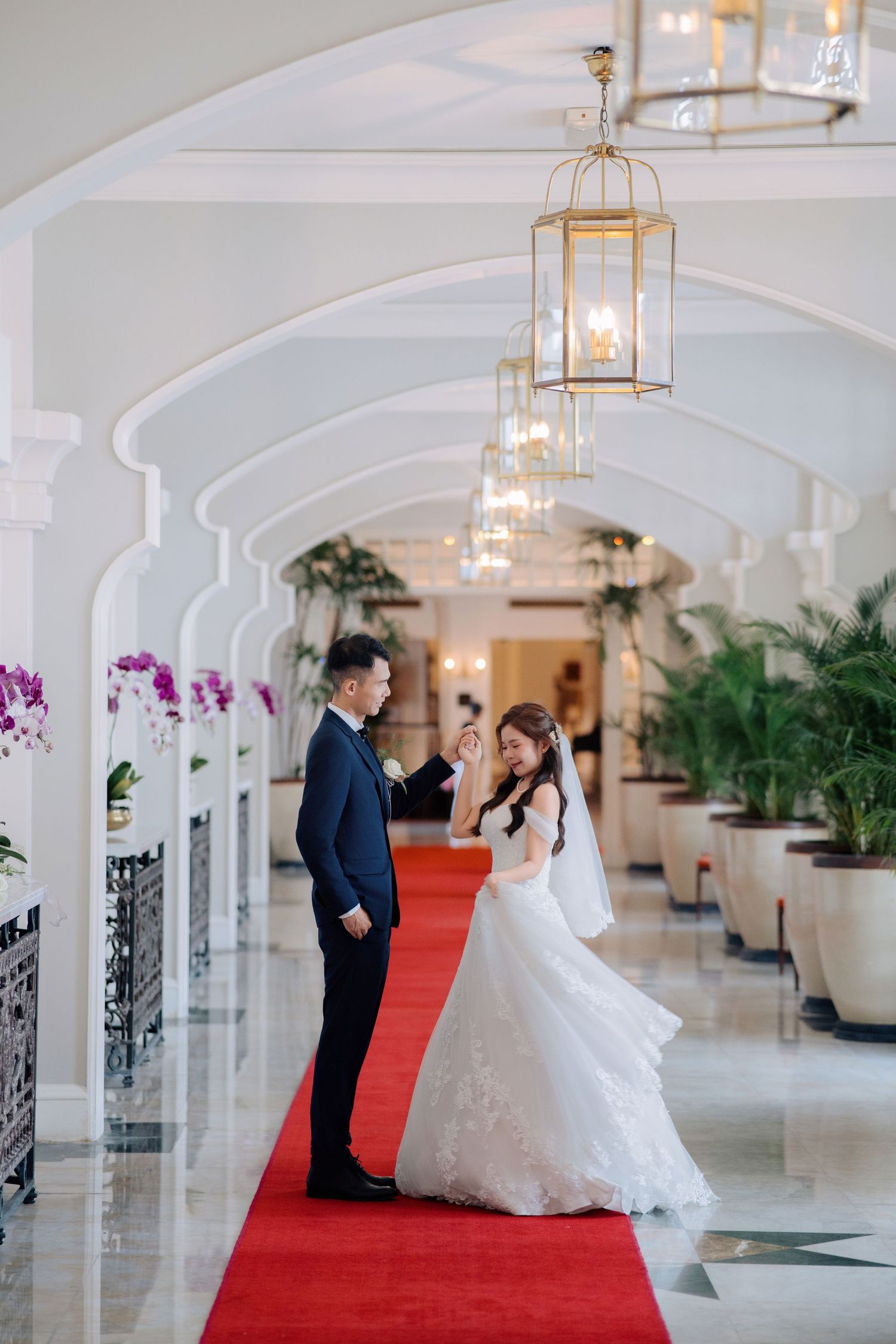 Elegant wedding couple dancing in grand hallway with ornate lighting and red carpet at Eastern & Oriental Hotel (E&O).