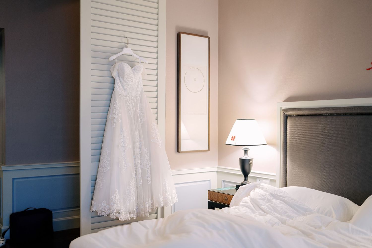 A lace A-line wedding dress hanging in a bridal suite, showcasing intricate floral embroidery and a classic silhouette