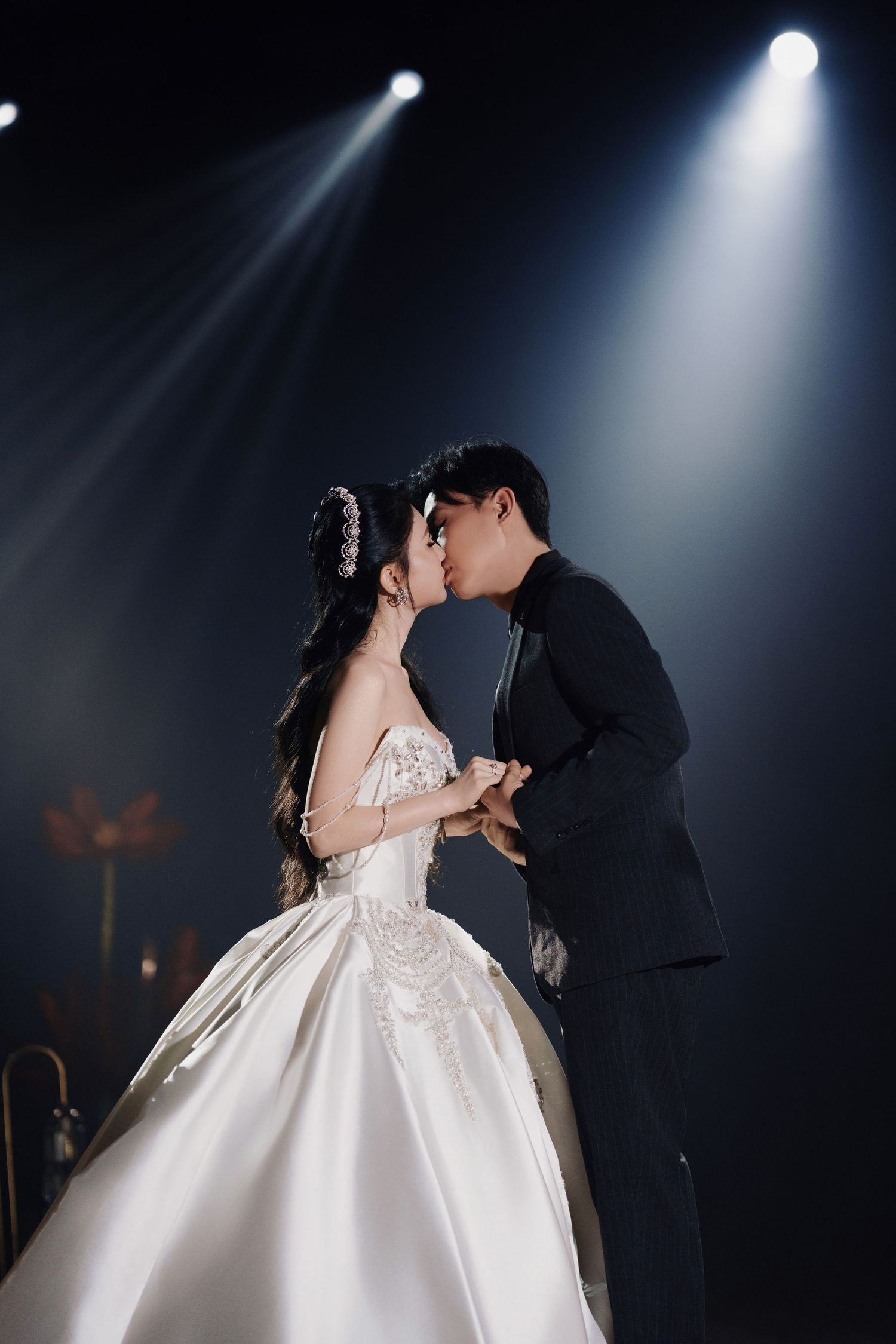 Bride and groom kissing under a bright white spotlight against a dark, atmospheric background