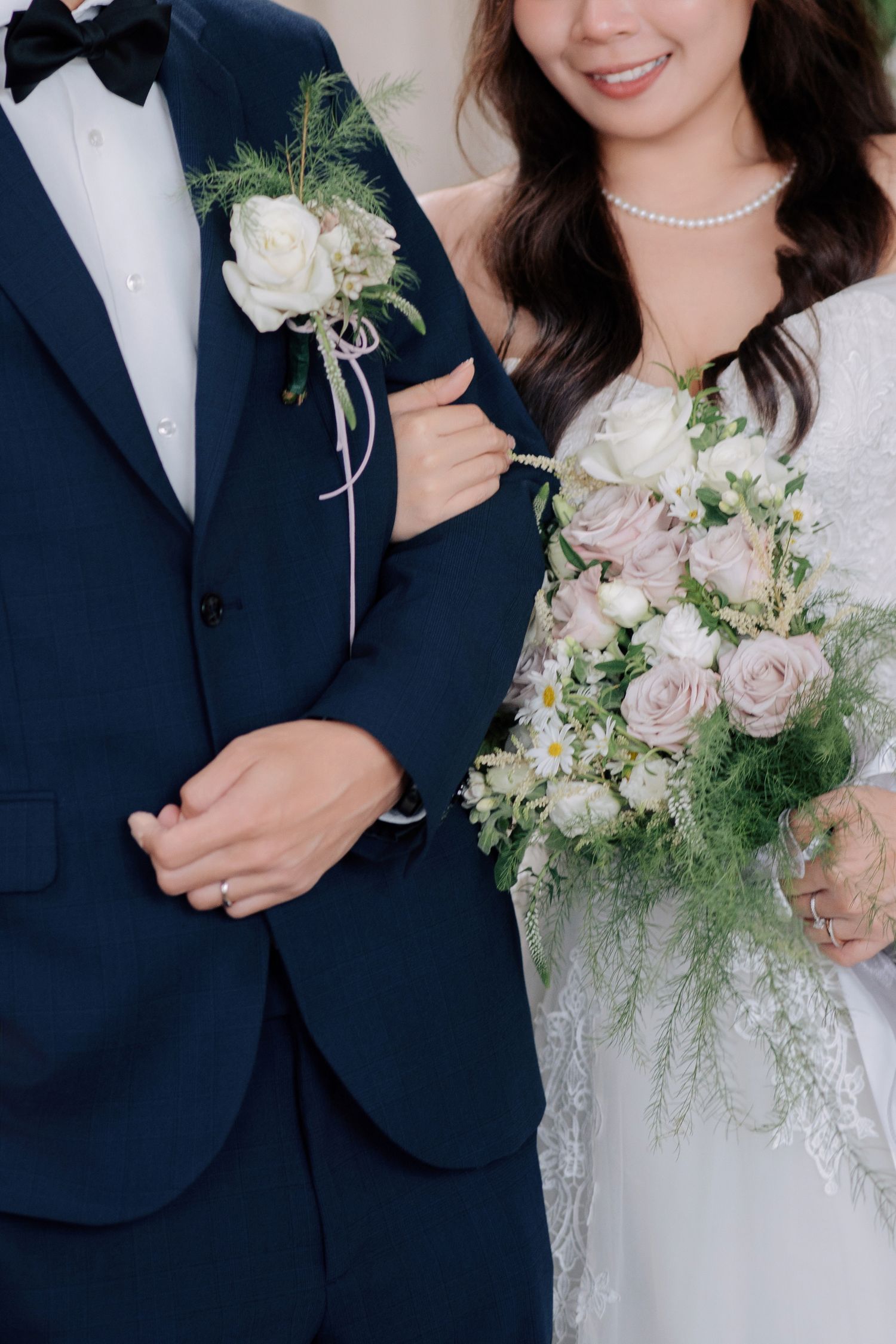 Bridal bouquet with dusty pink roses and greenery held next to groom's white rose boutonniere