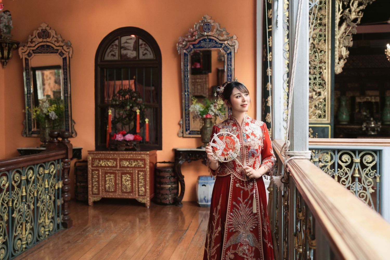 Bride in a stunning red Qun Kwa holding a traditional wedding fan in a Peranakan-style interior