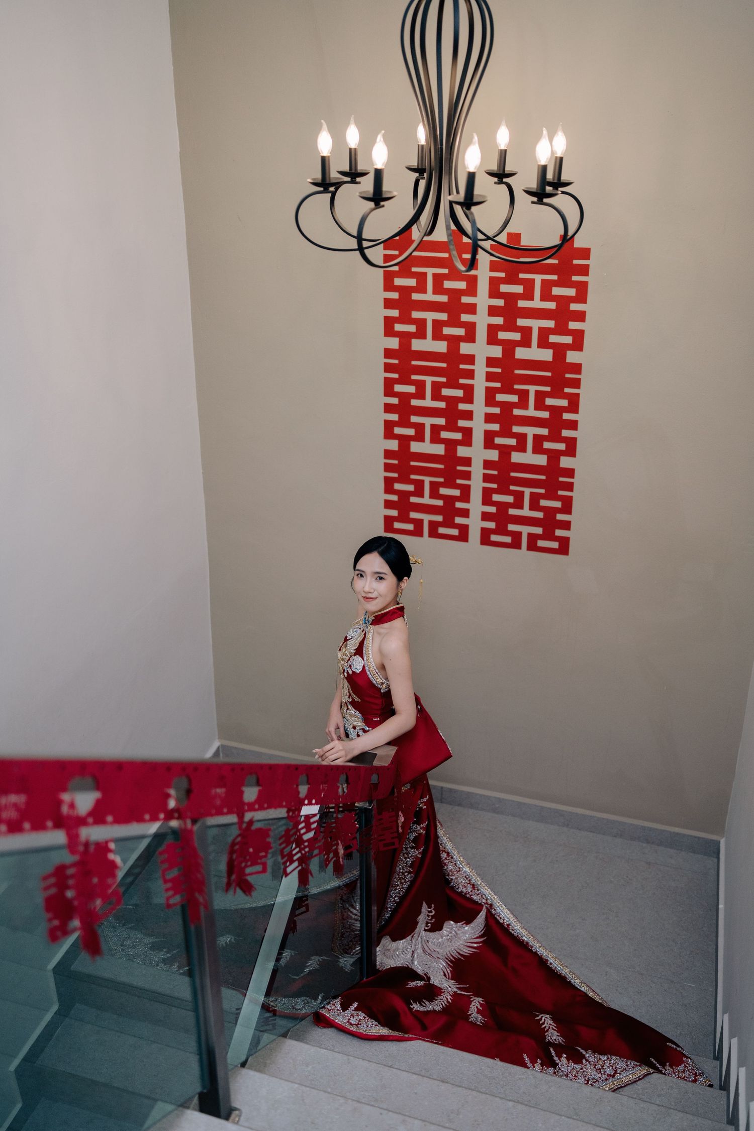 A bride poses on stairs in a red embroidered gown, a perfect look for a Traditional Chinese Wedding