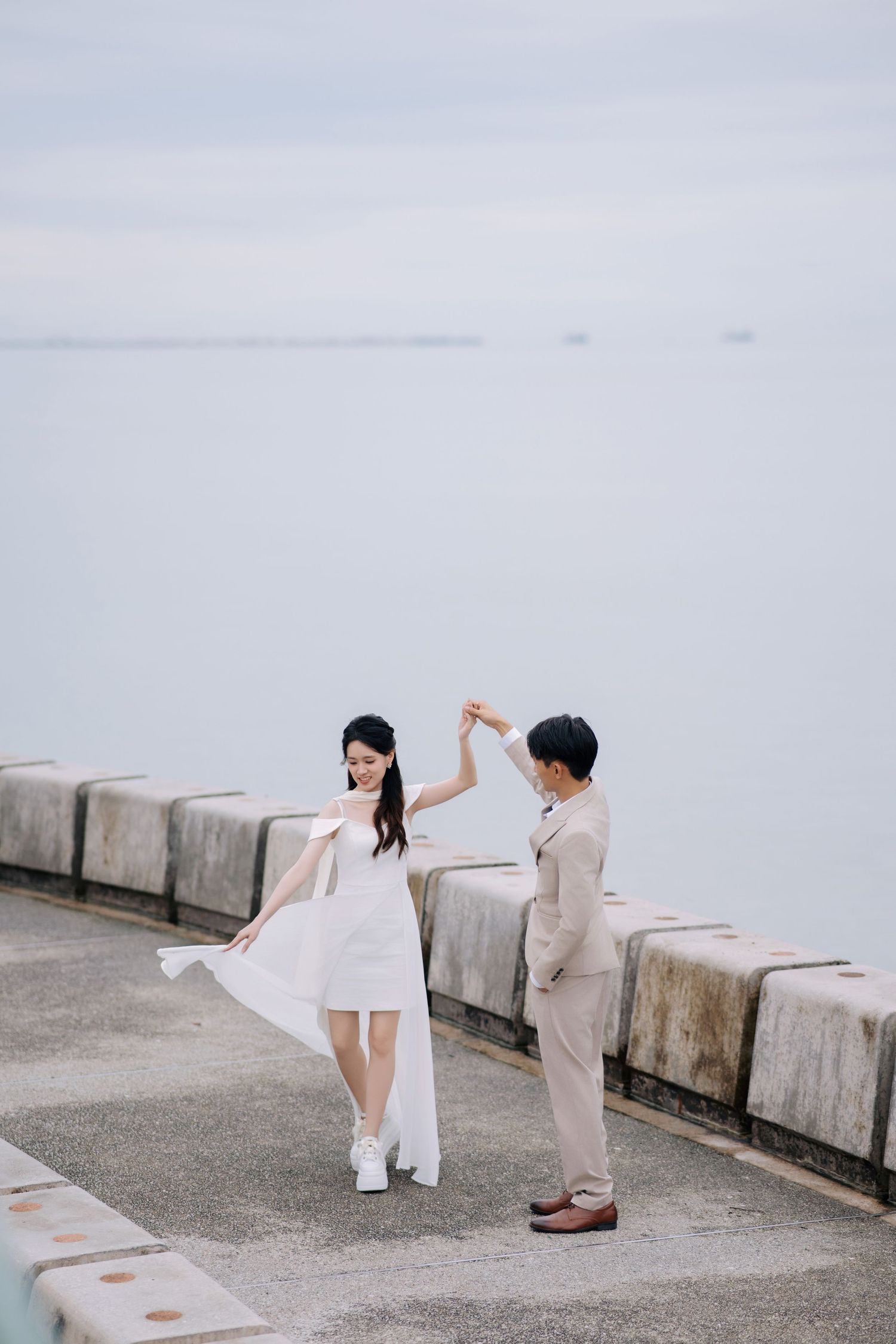 Creative wedding poses captured along concrete barriers by the sea.