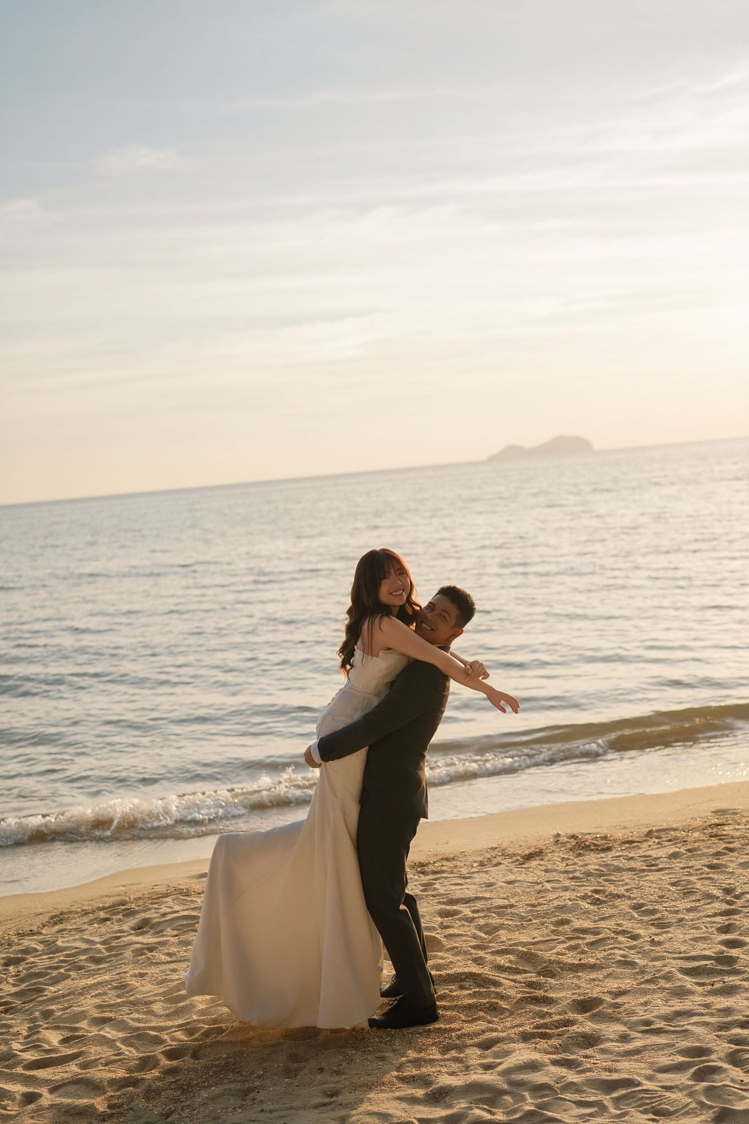 Joyful wedding couple embracing on a beach at sunset.