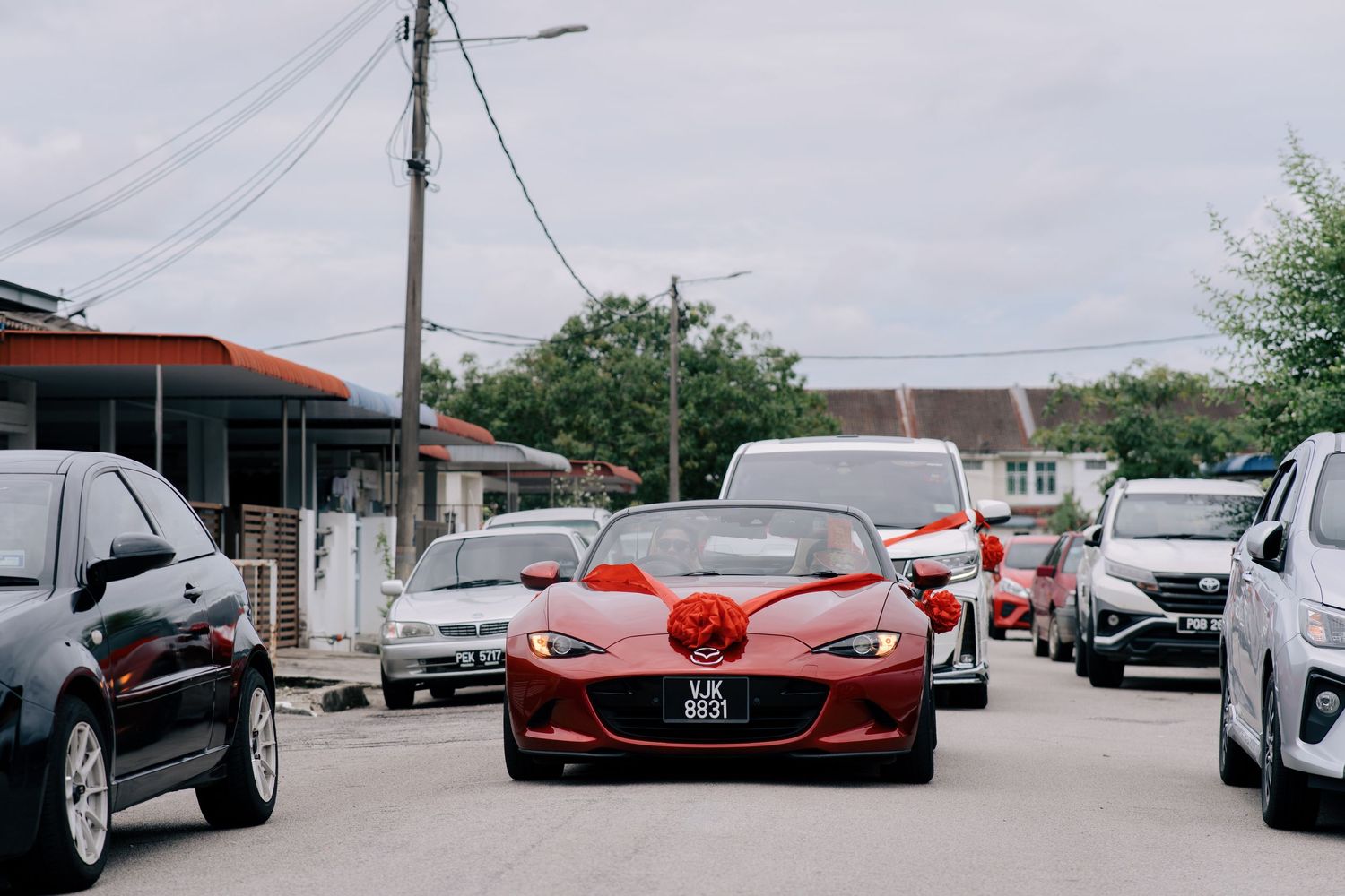Red Mazda convertible decorated with a large red ribbon leading a wedding car convoy