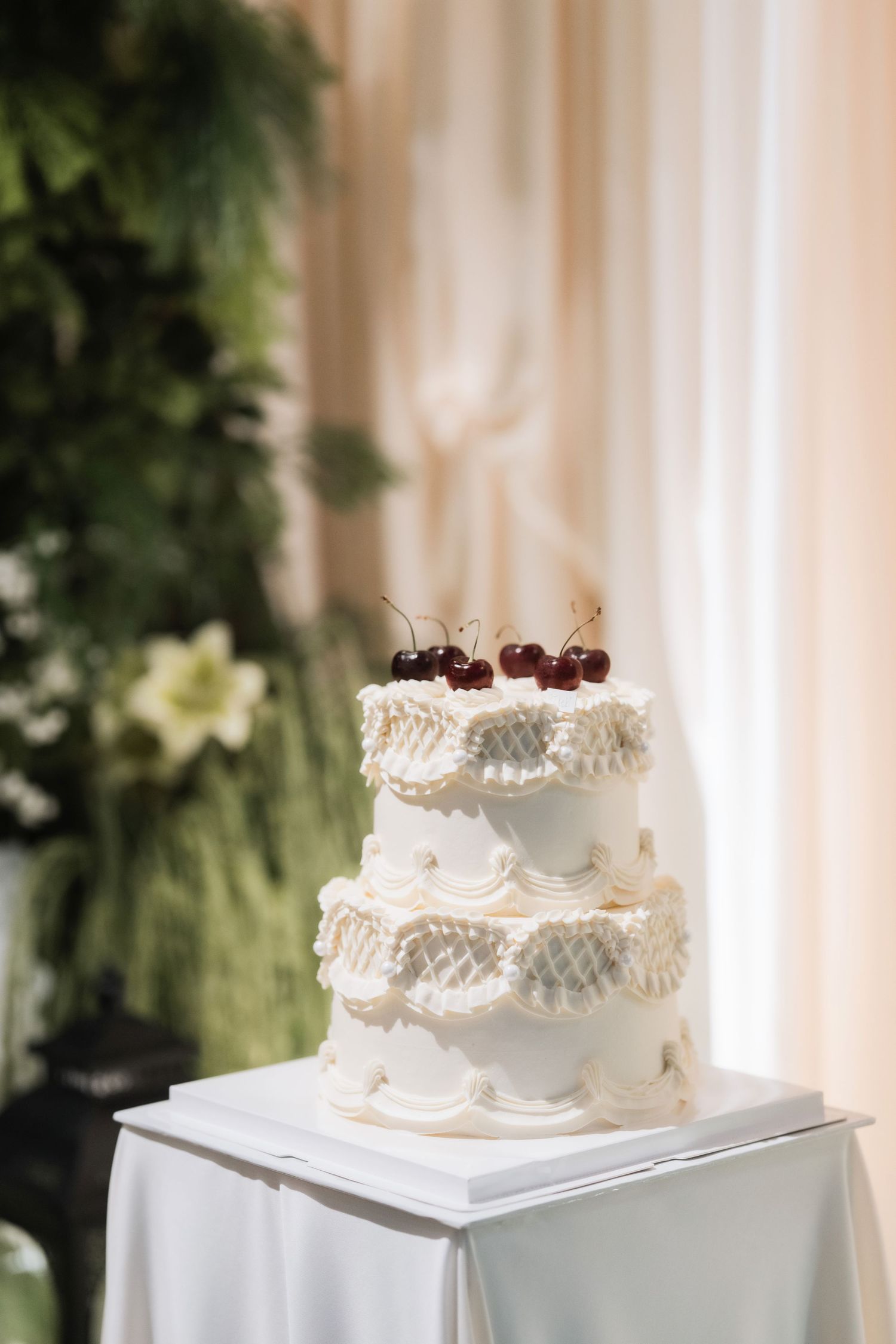 An elegant white wedding cake displayed on pedestals with delicate frosting details.