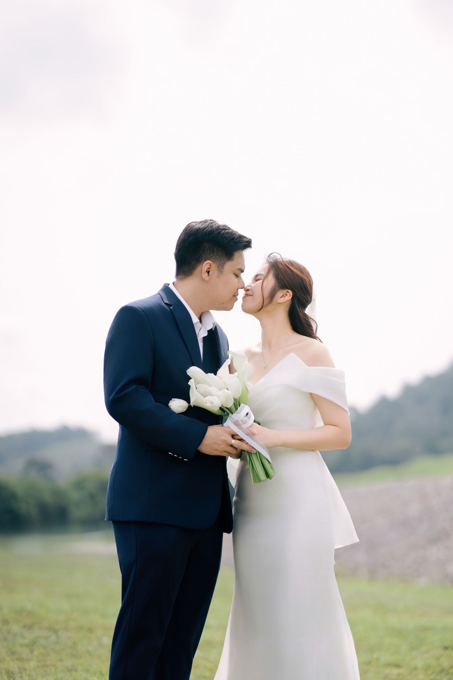 A romantic moment between newlyweds holding white flowers in an outdoor setting.