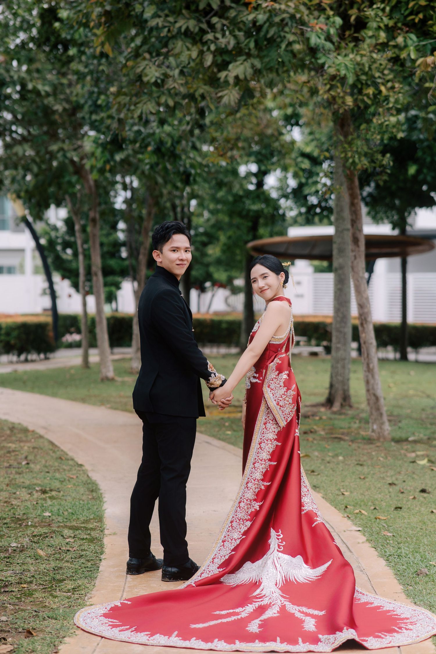 Bride in a red phoenix-embroidered gown and groom in a Tang-style suit looking back during their traditional Chinese wedding