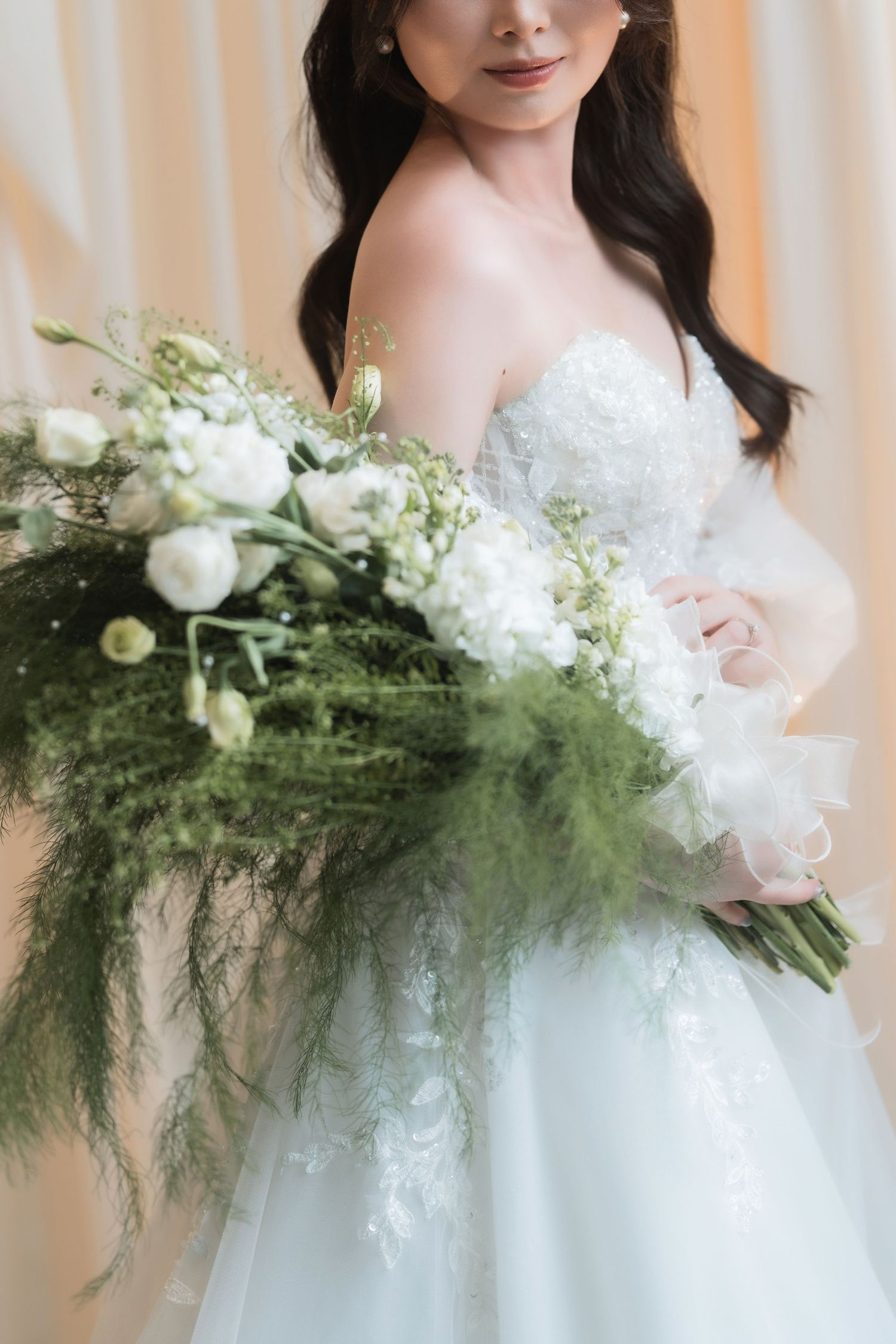 Elegant bridal bouquet with white roses and cascading greenery against white gown.