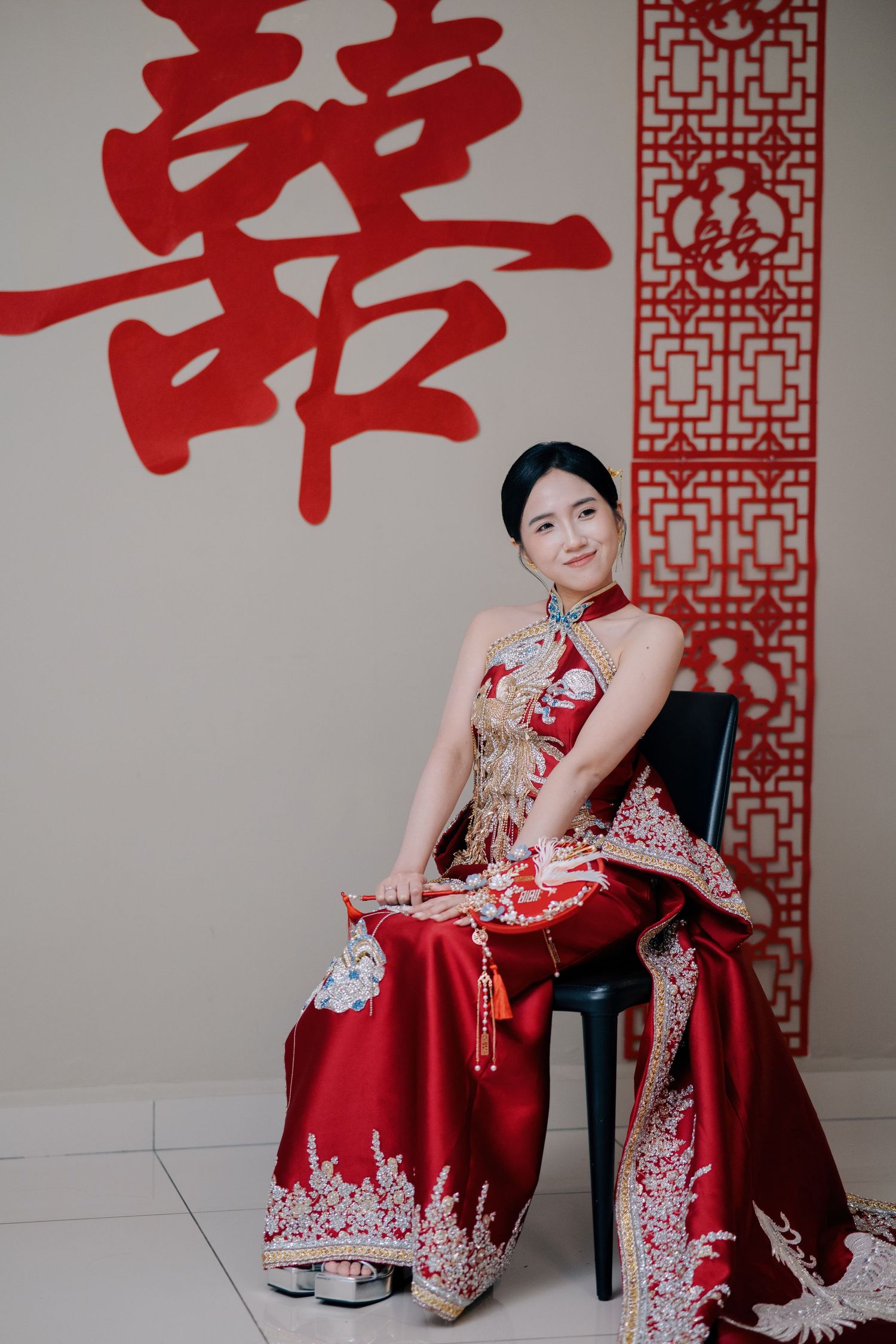 Bride in a red embroidered wedding gown sits before a Double Happiness sign