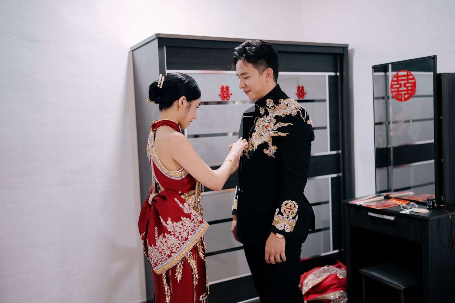 Bride adjusting the groom's dragon robe before their traditional Chinese wedding ceremony