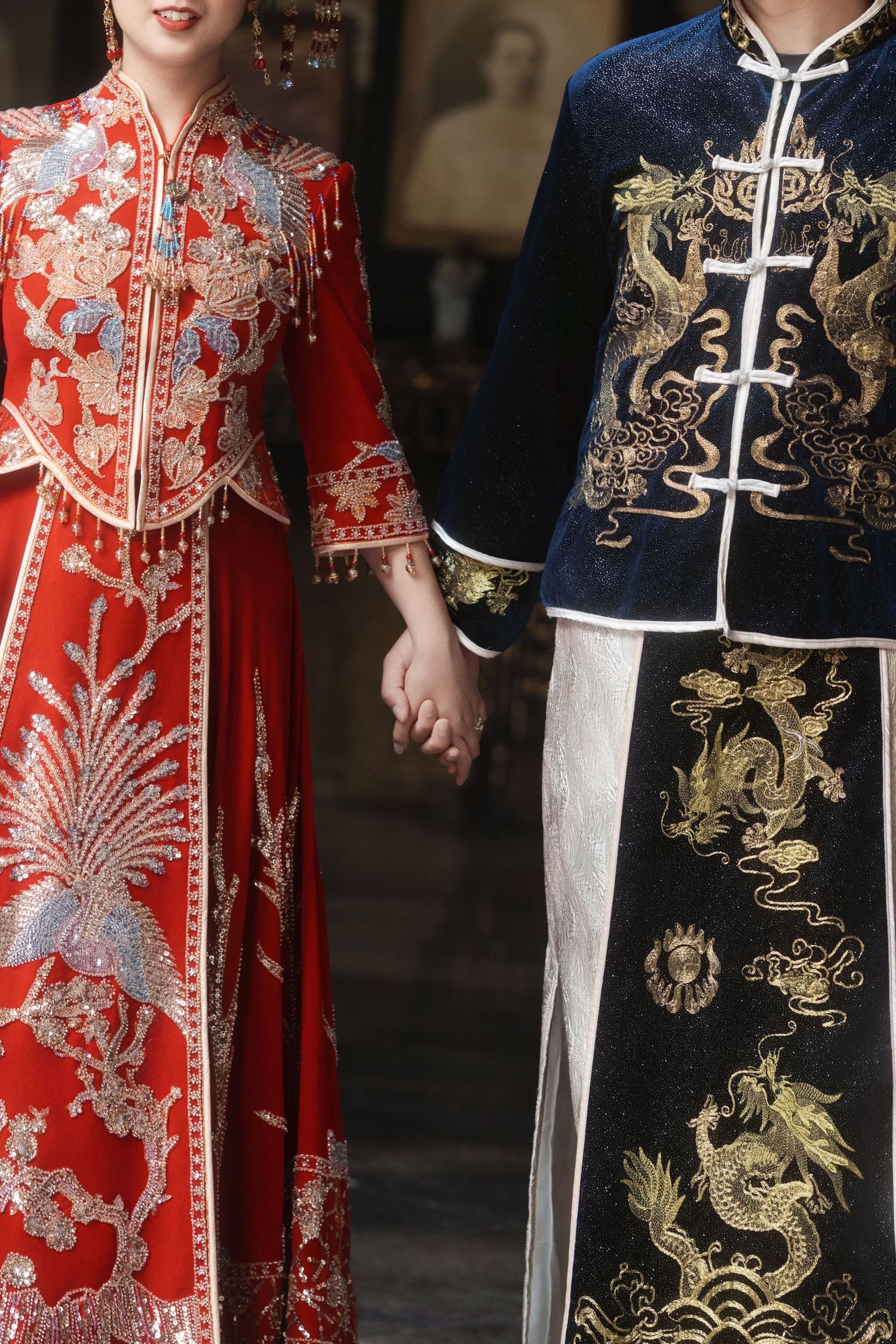 Close-up of a bride and groom holding hands, highlighting the embroidery of their traditional Chinese wedding attire