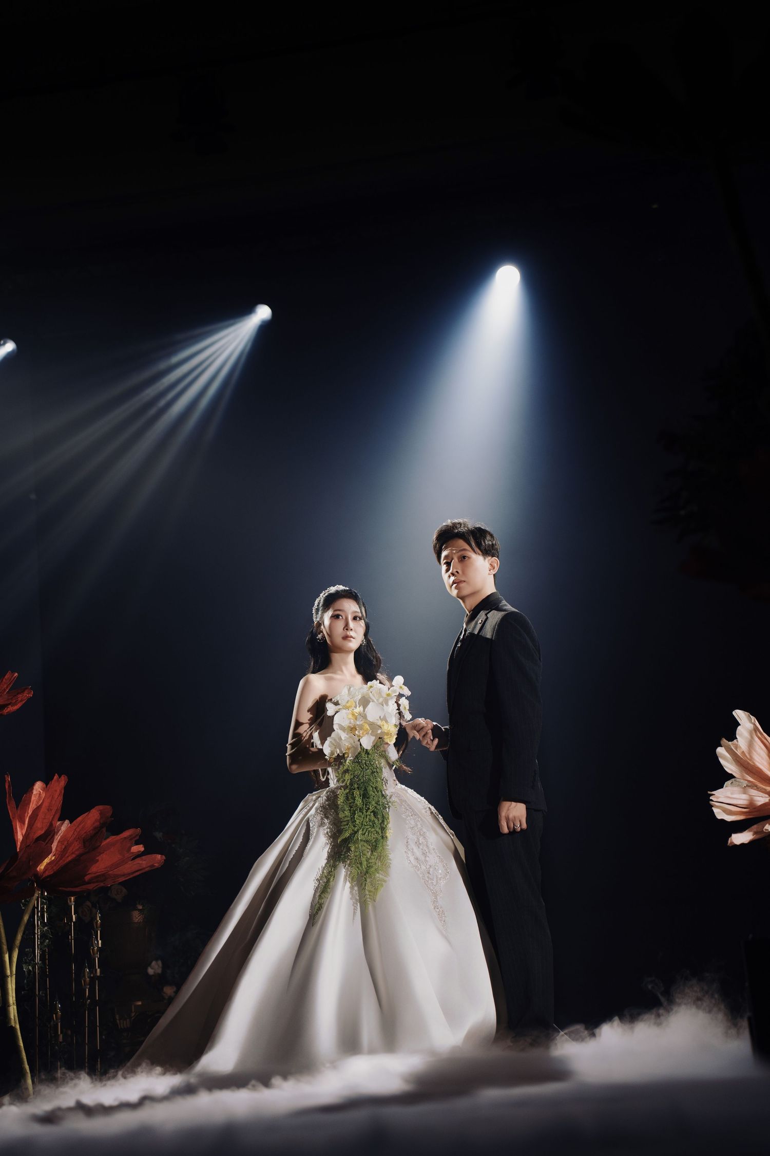 Bride and groom posing on a fog-covered stage during an enchanted forest wedding reception