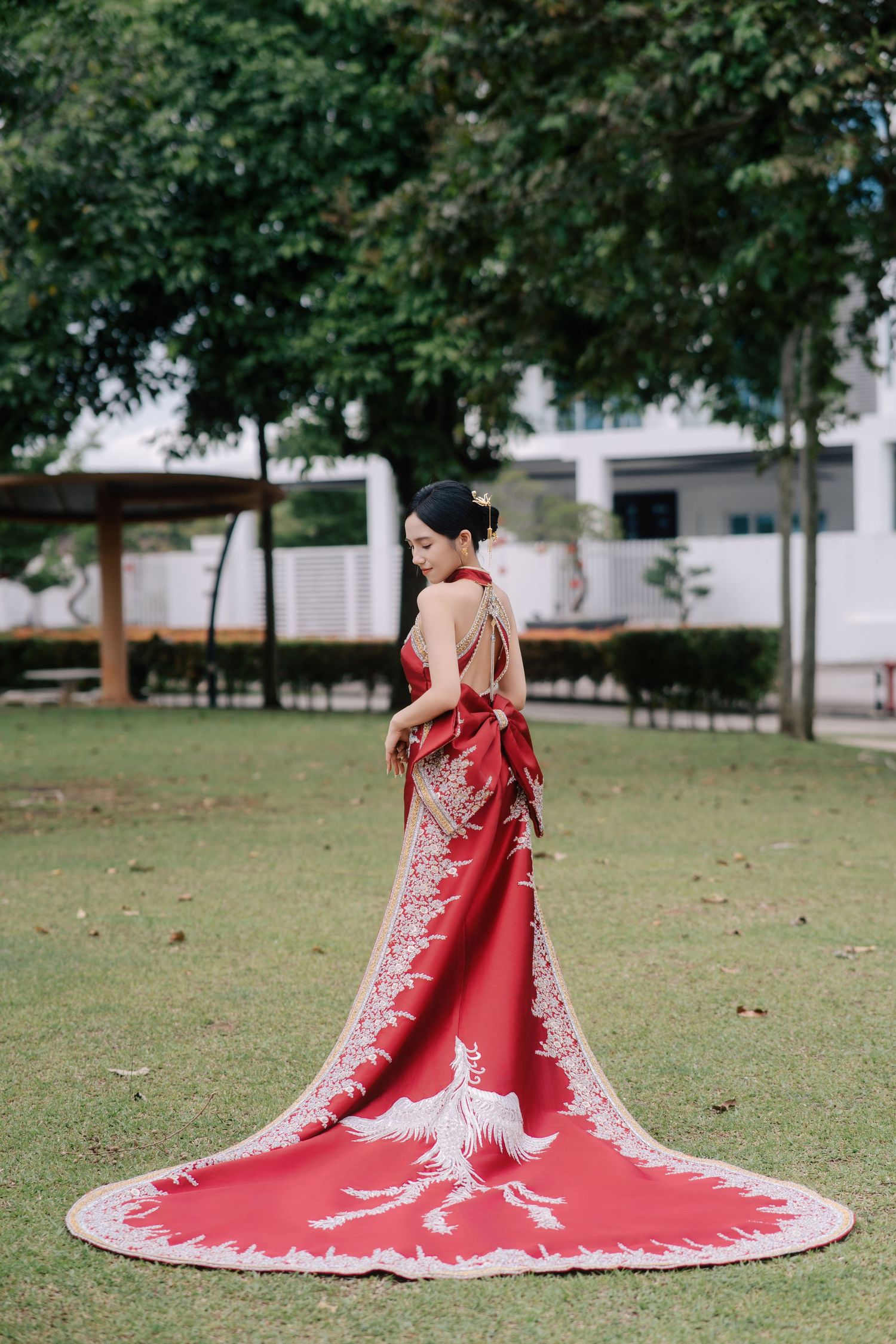 Bride standing alone in a field, looking over her shoulder to show the full length of her red phoenix-embroidered train