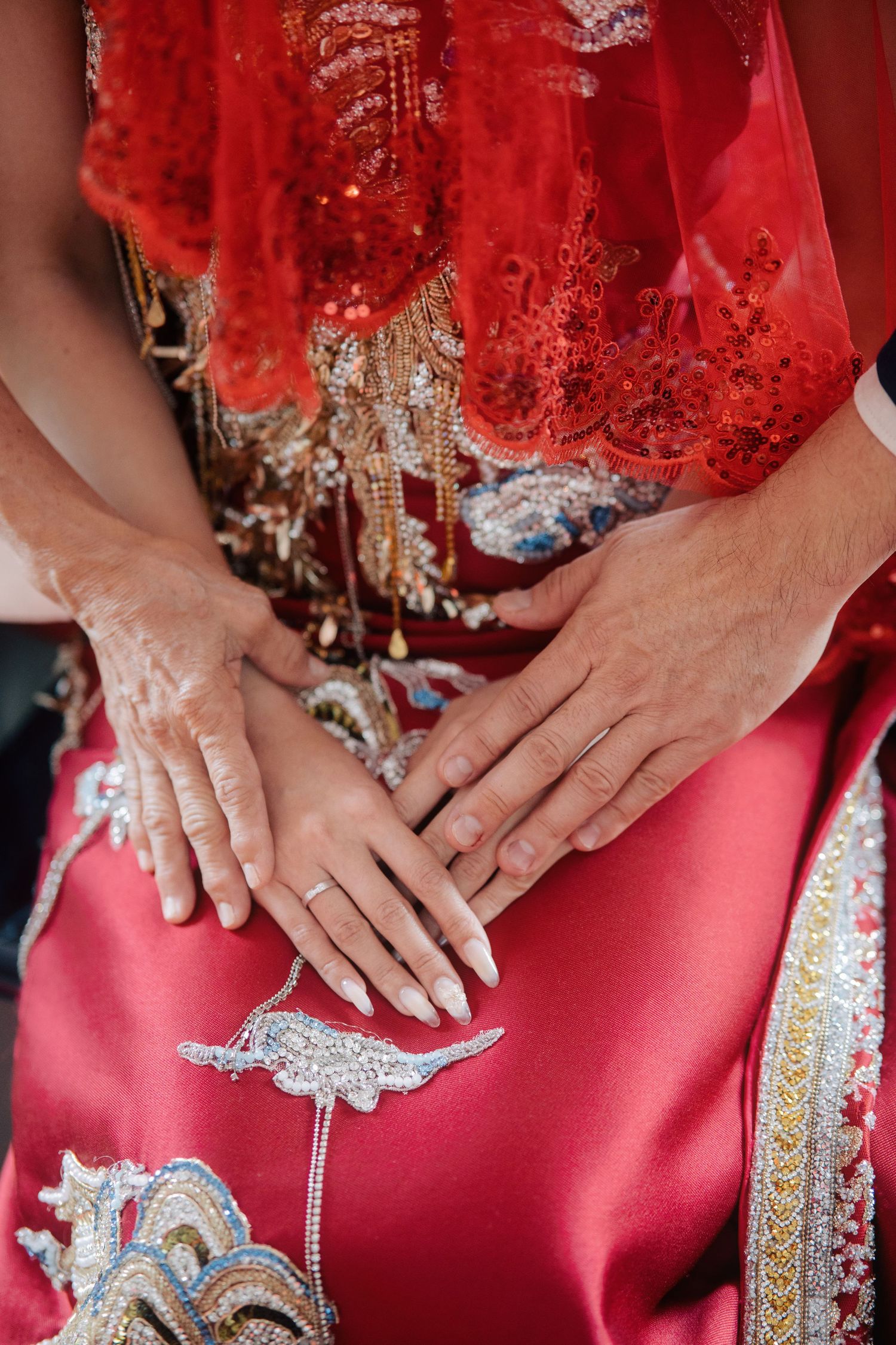 Close-up of a bride’s hands with a silver ring resting on a red silk dress with intricate gold and silver embroidery