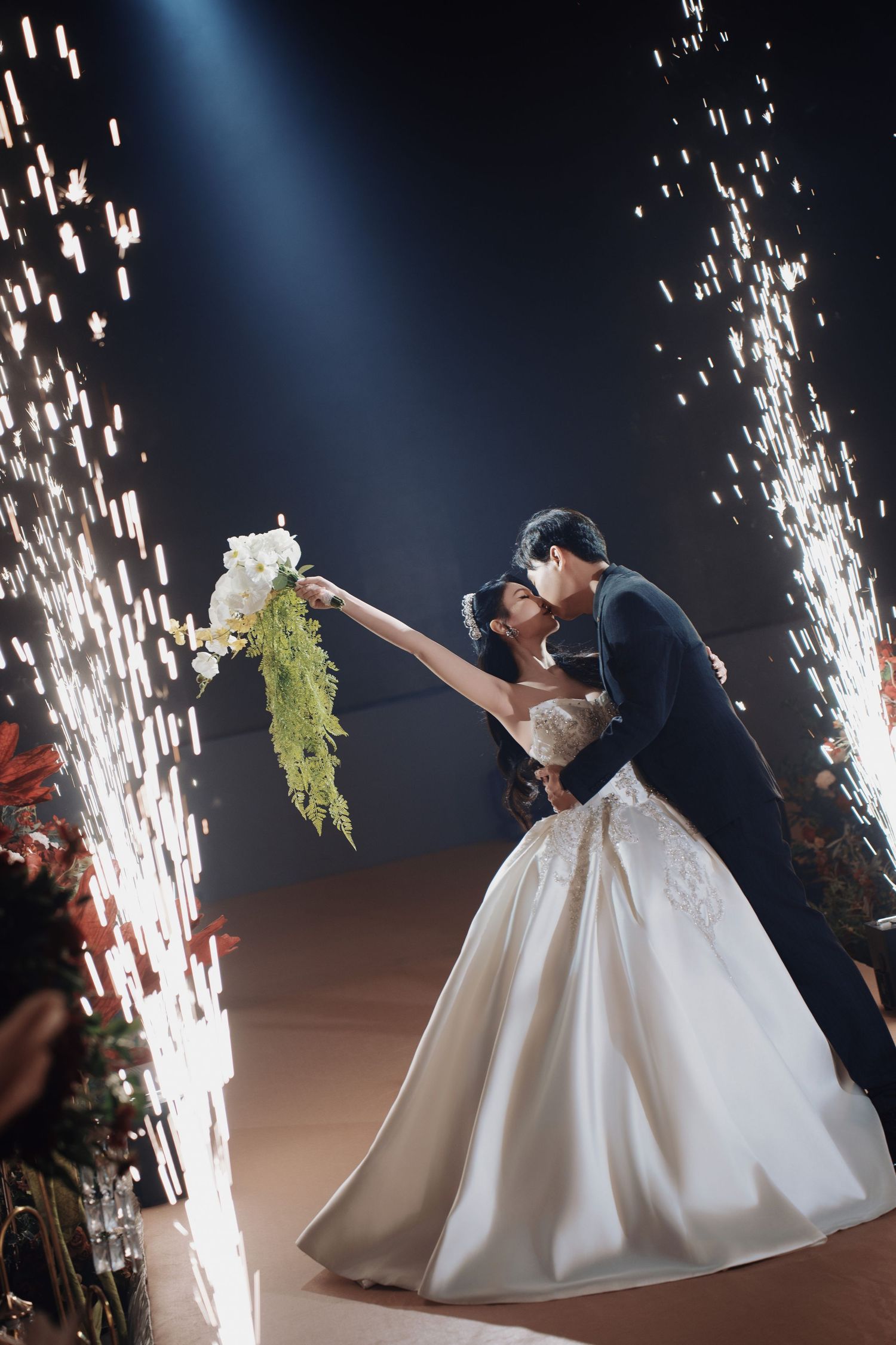 Couple kissing during a grand entrance with indoor sparks and fairytale ballroom lighting