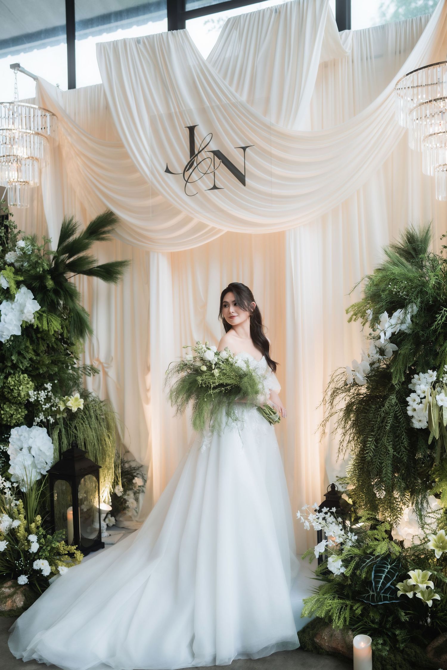 Bride in white gown poses under draped fabric backdrop with elegant floral decorations.