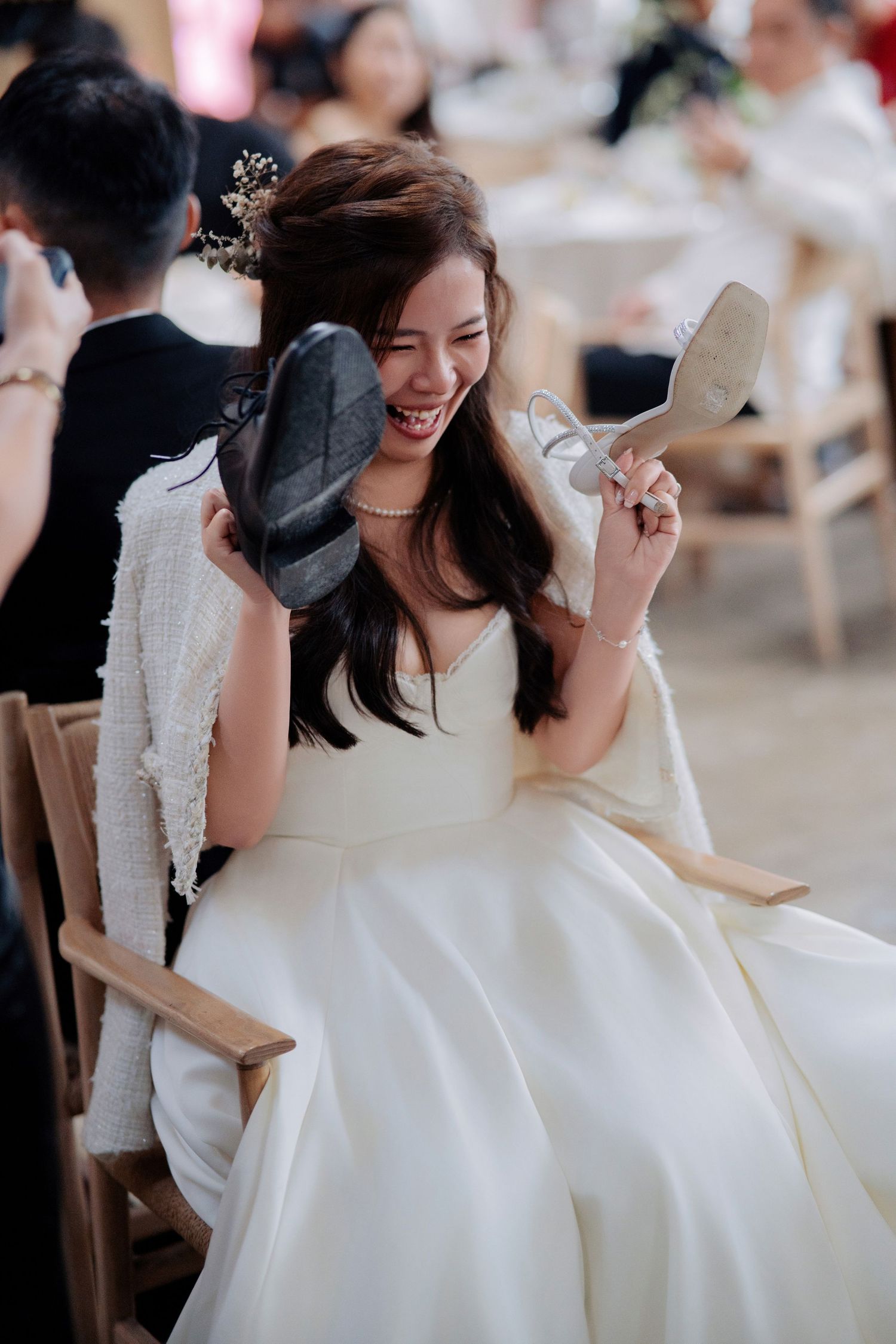 Close-up of the bride laughing heartily while holding both a dress shoe and a sparkling high heel