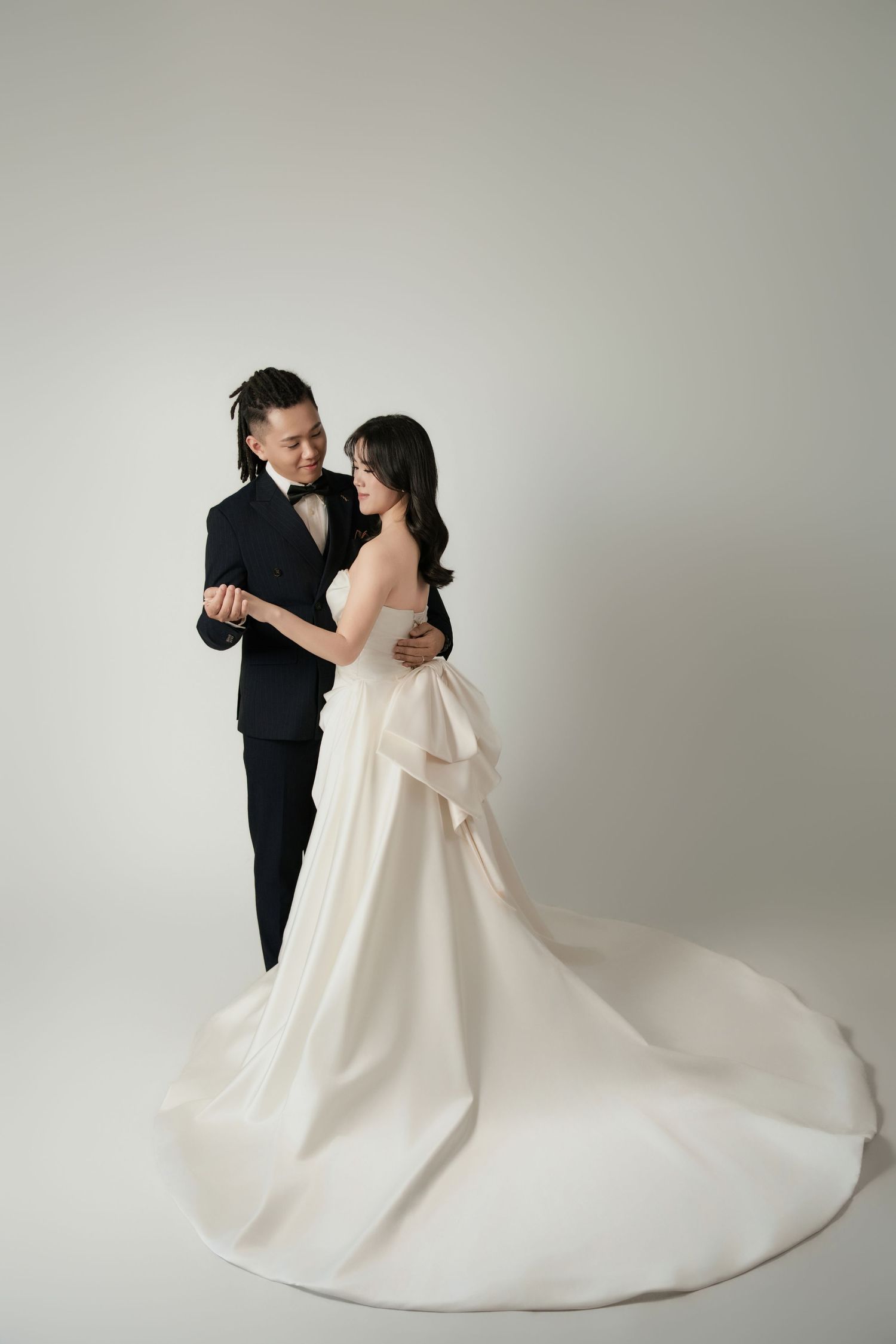 Couple sharing a tender moment in pre-wedding photoshoot studio portrait, bride in bow-back ball gown, groom in tuxedo
