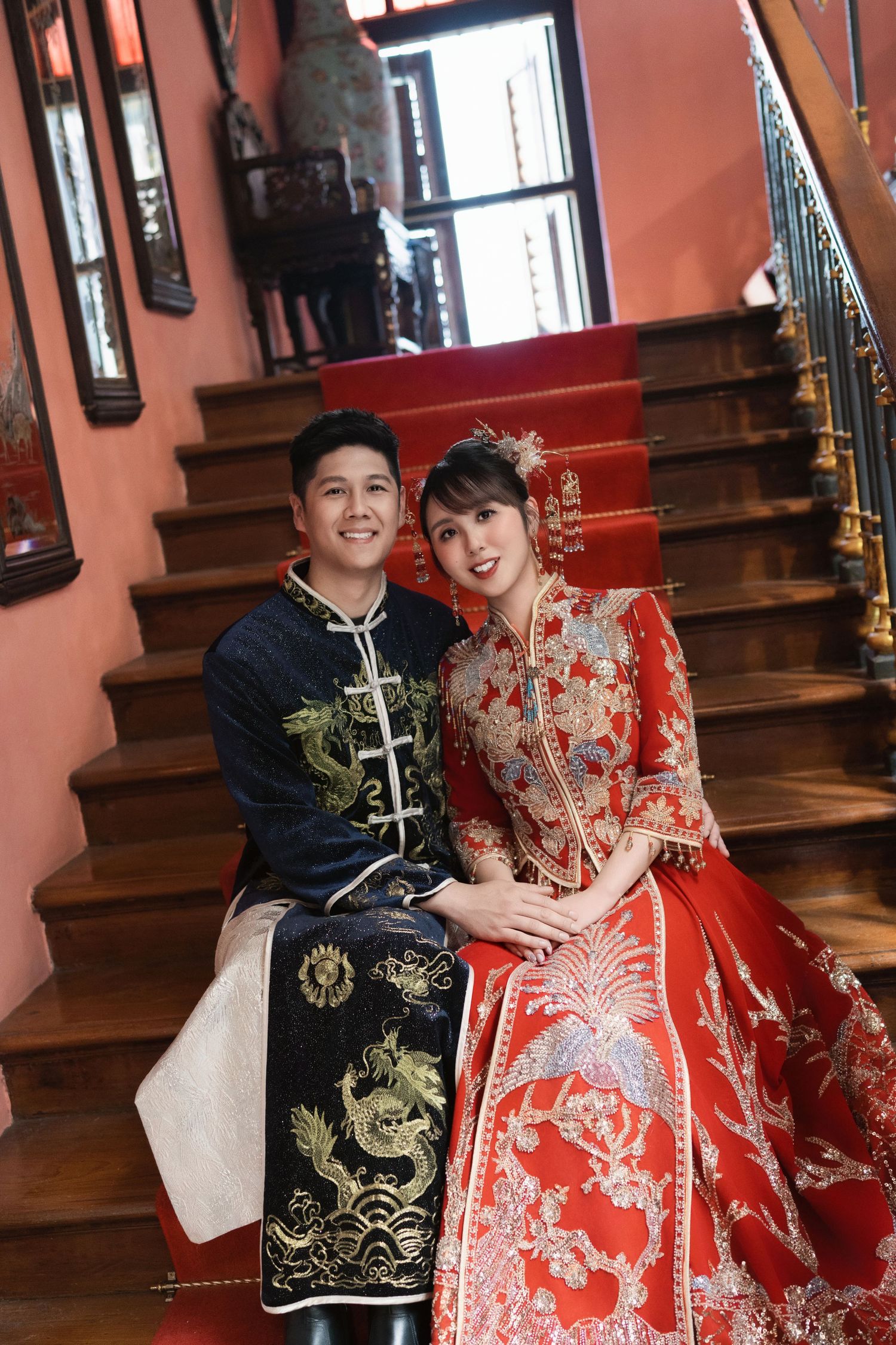 Couple in intricate Chinese wedding garments sitting on the staircase of a heritage Peranakan house