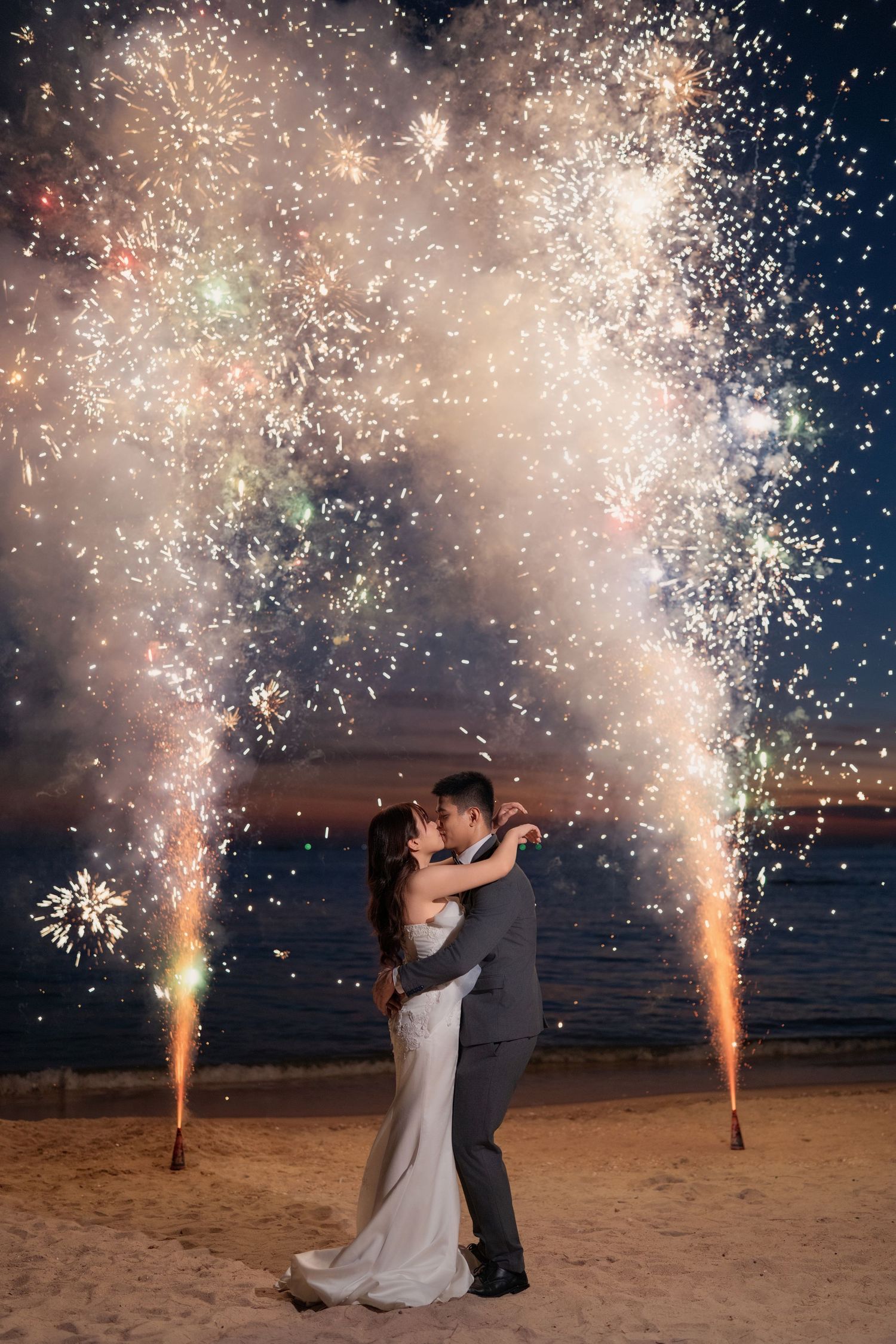 Romantic beach wedding scene with sparklers creating magical light effects during sunset celebrations.
