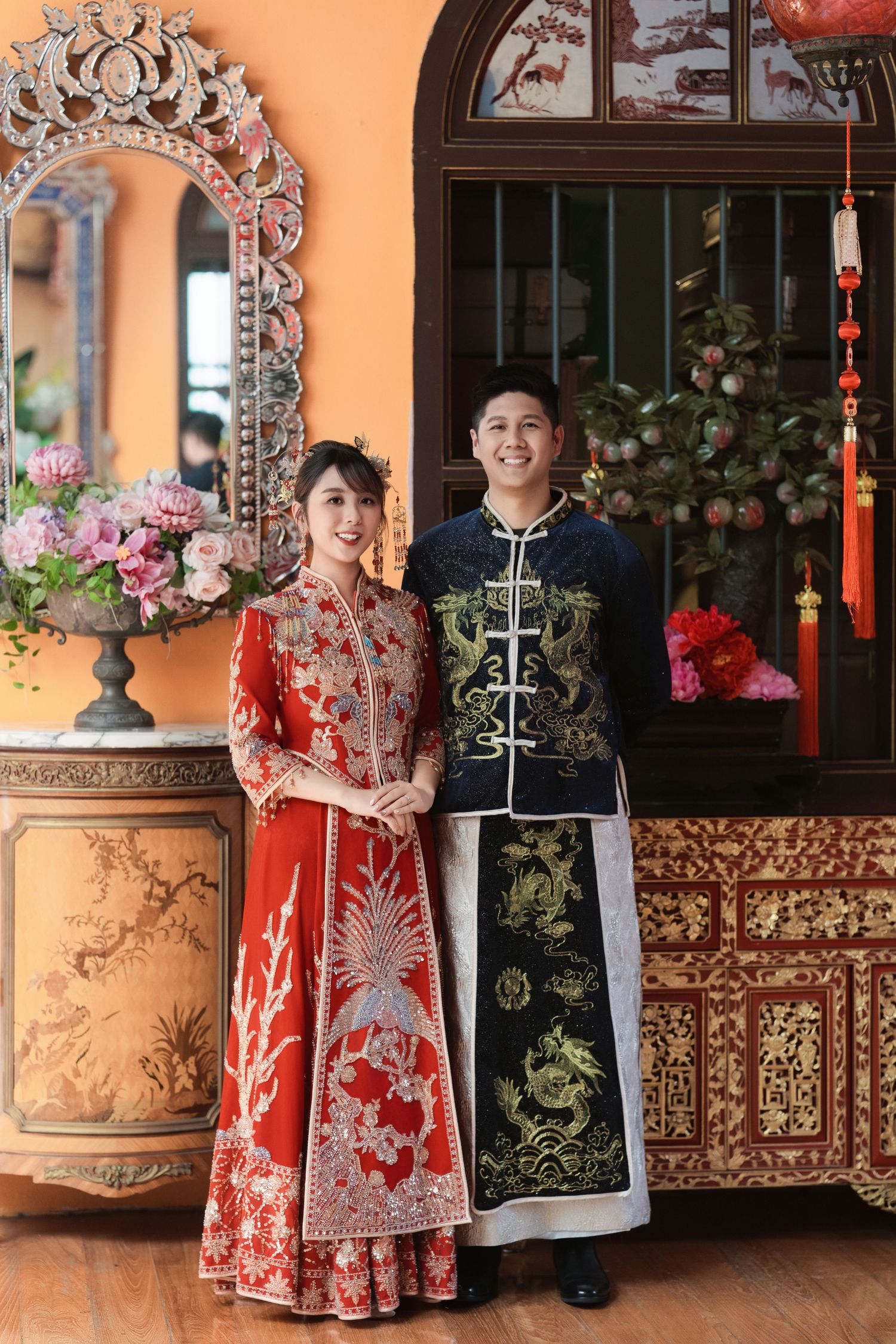 Formal wedding portrait of a couple in traditional red and navy silk robes inside a historic Malaysian mansion