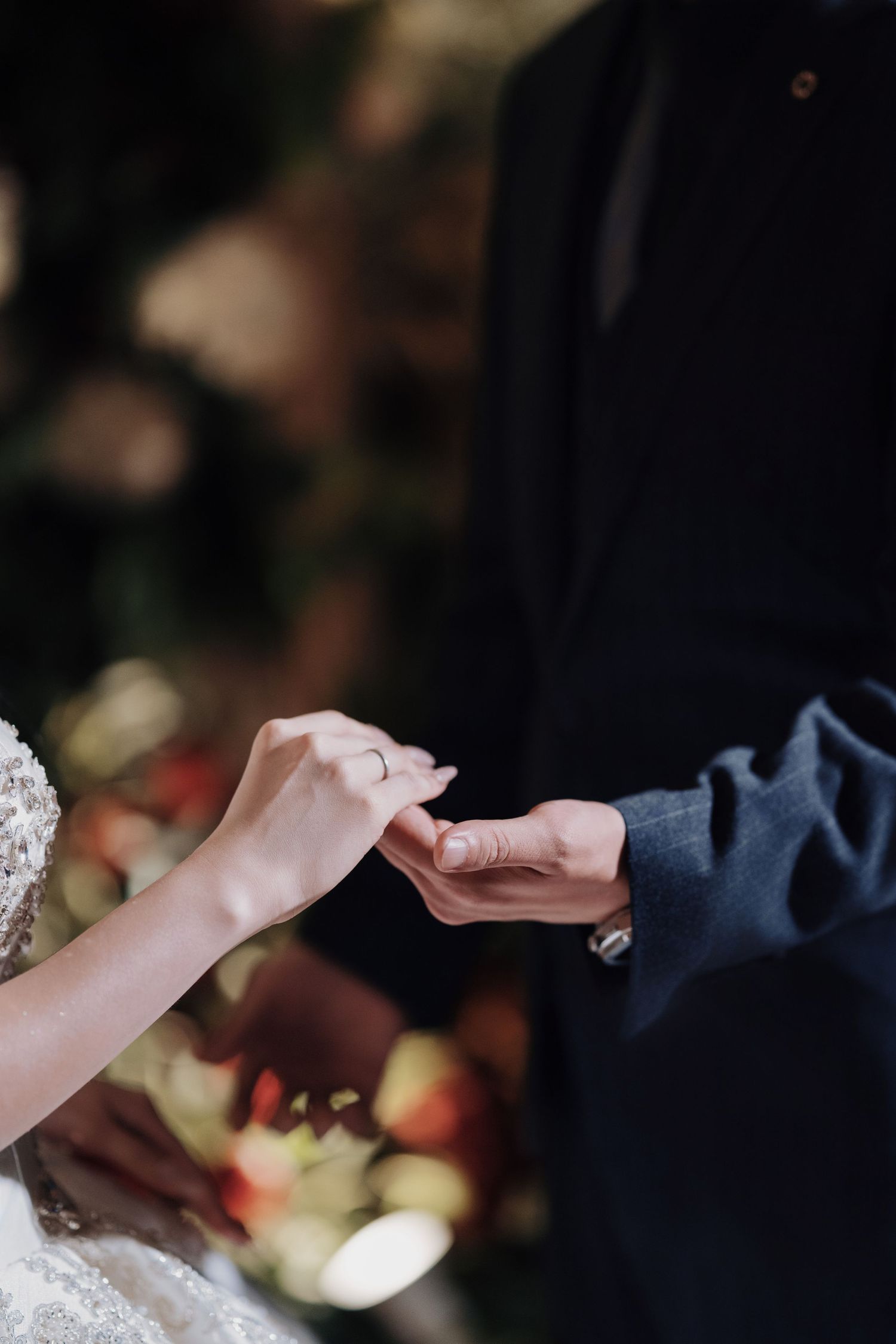 Intimate close-up of a bride and groom holding hands, highlighting the wedding ring and suit sleeve