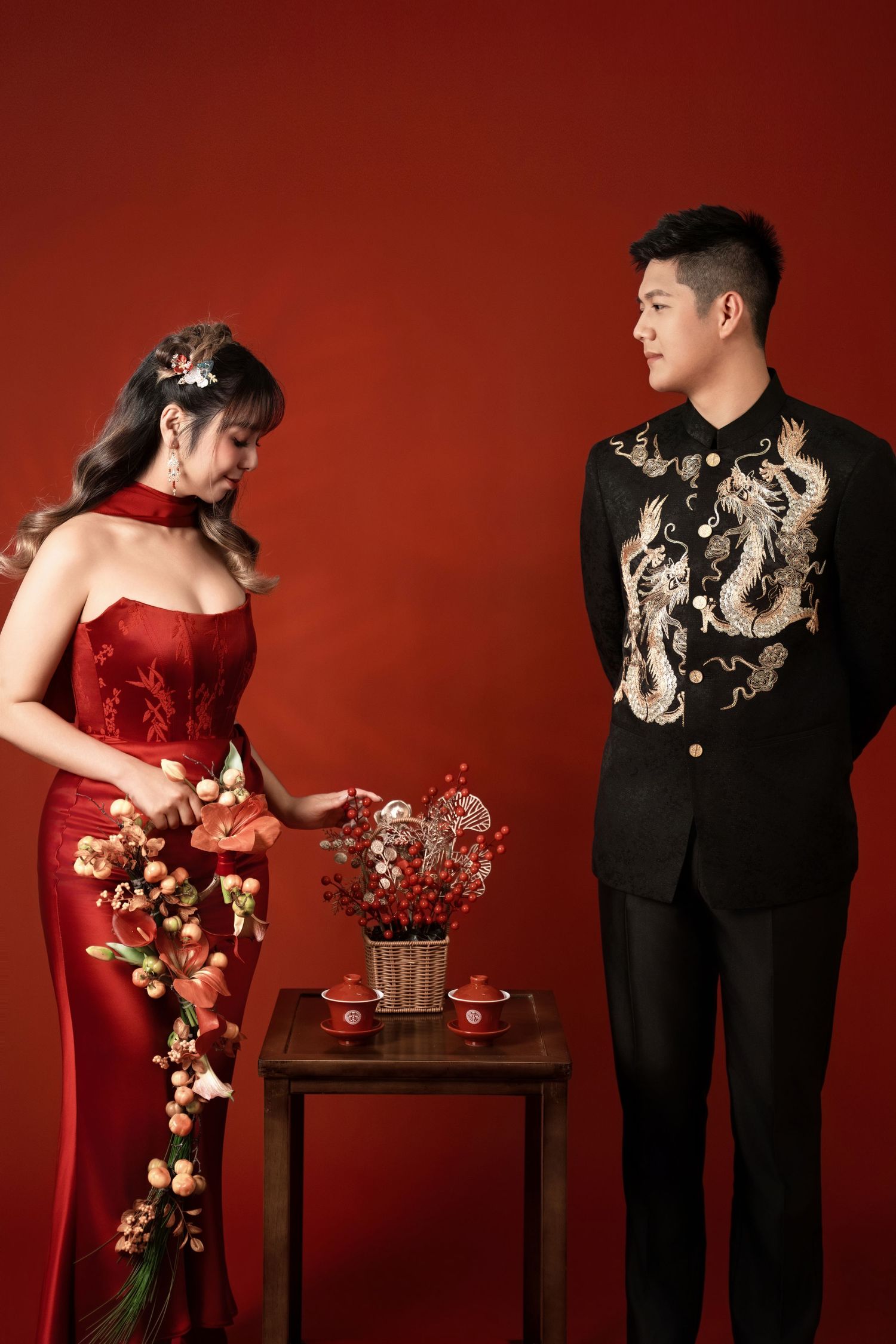 Romantic studio portraits against red backdrop featuring traditional Chinese wedding attire and decor.