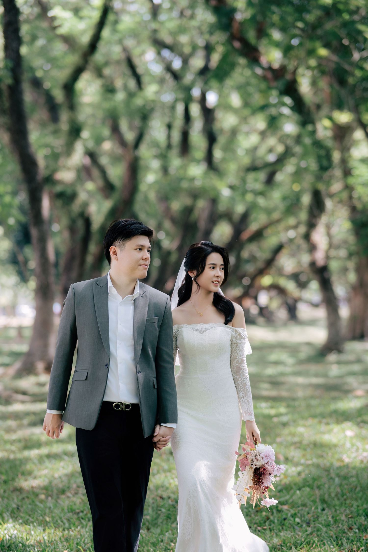 Elegant couple strolling through a wooded park in wedding attire.