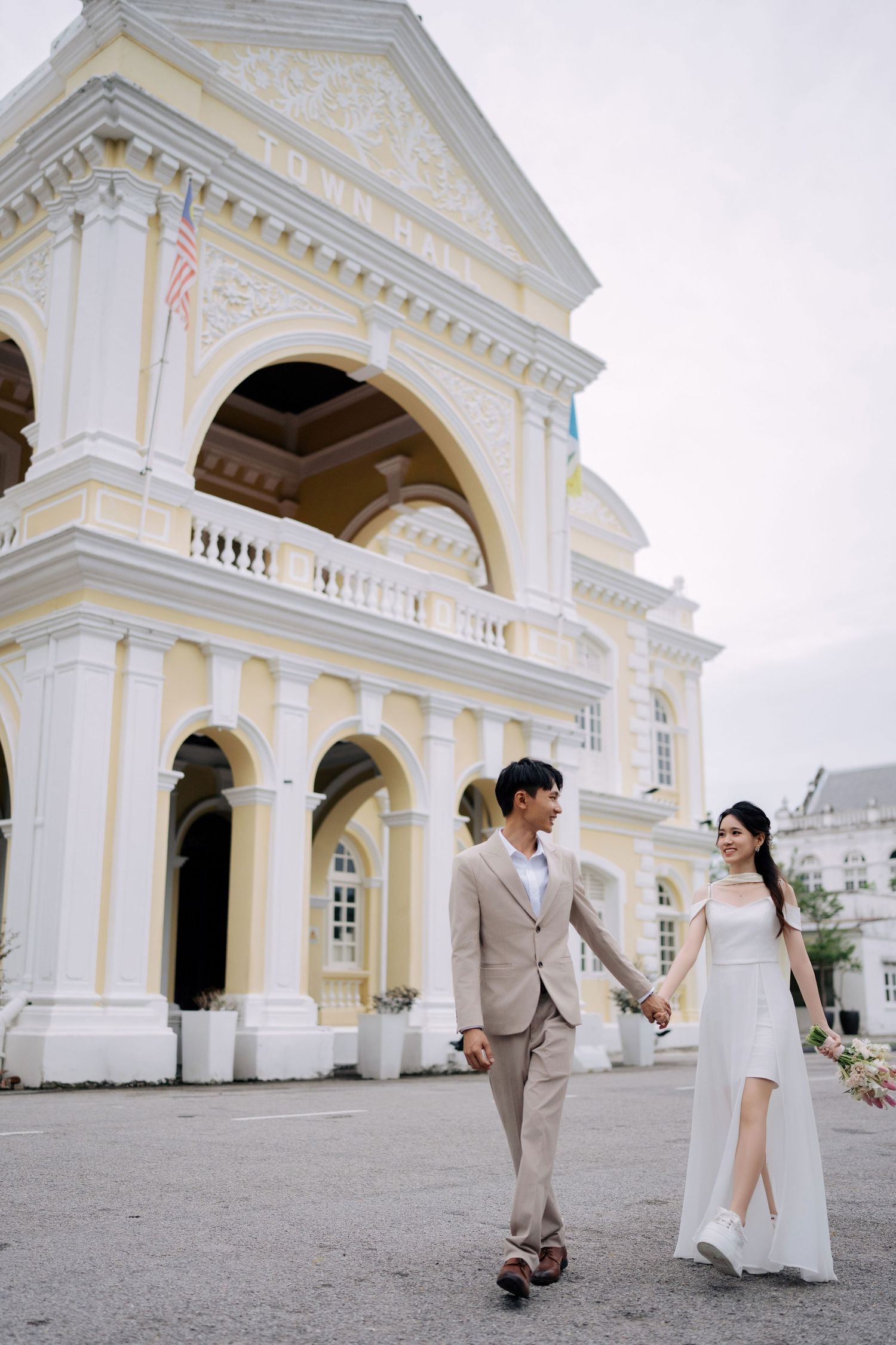 A couple poses for a George Town pre-wedding shoot in front of the iconic yellow colonial Town Hall architecture