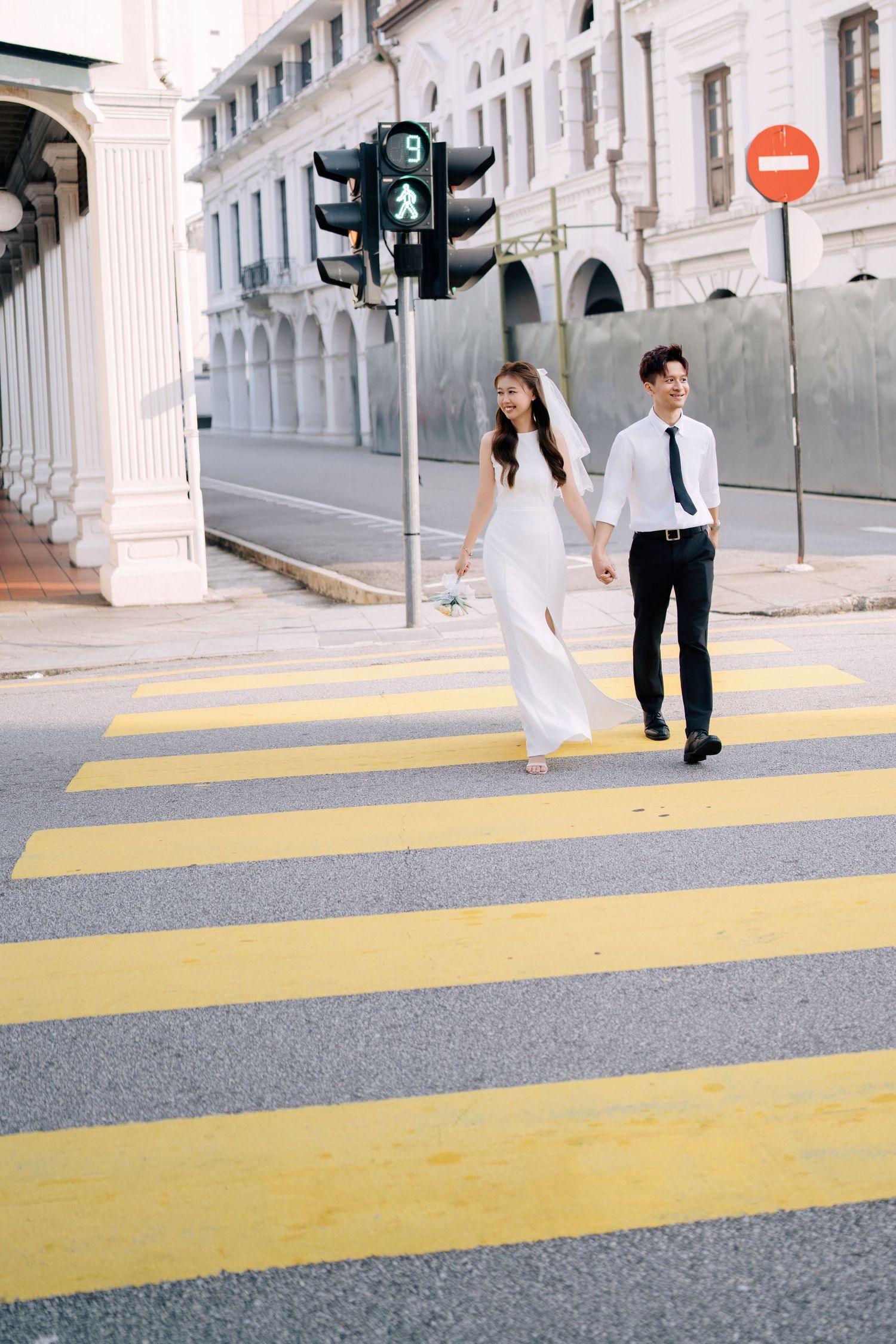 Urban wedding photoshoot of a couple crossing a city street with a green light and heritage architecture background