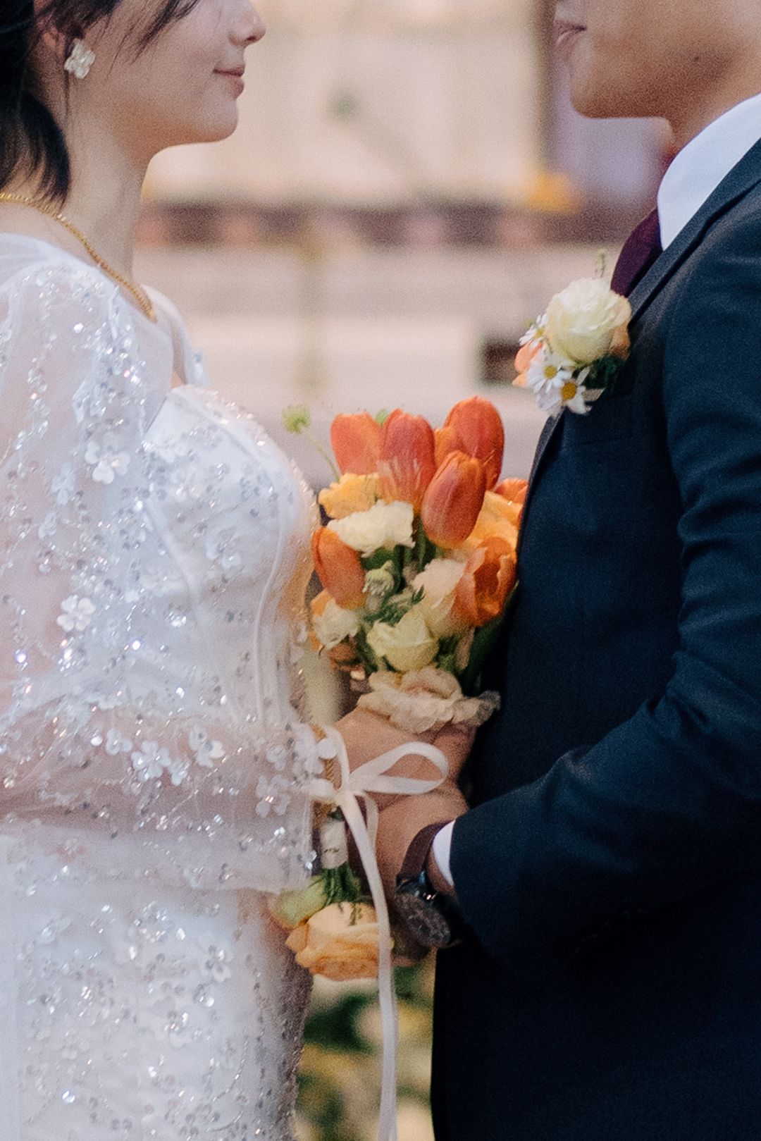 Close-up of a bride holding a bouquet of orange tulips and yellow roses while holding the groom's hand