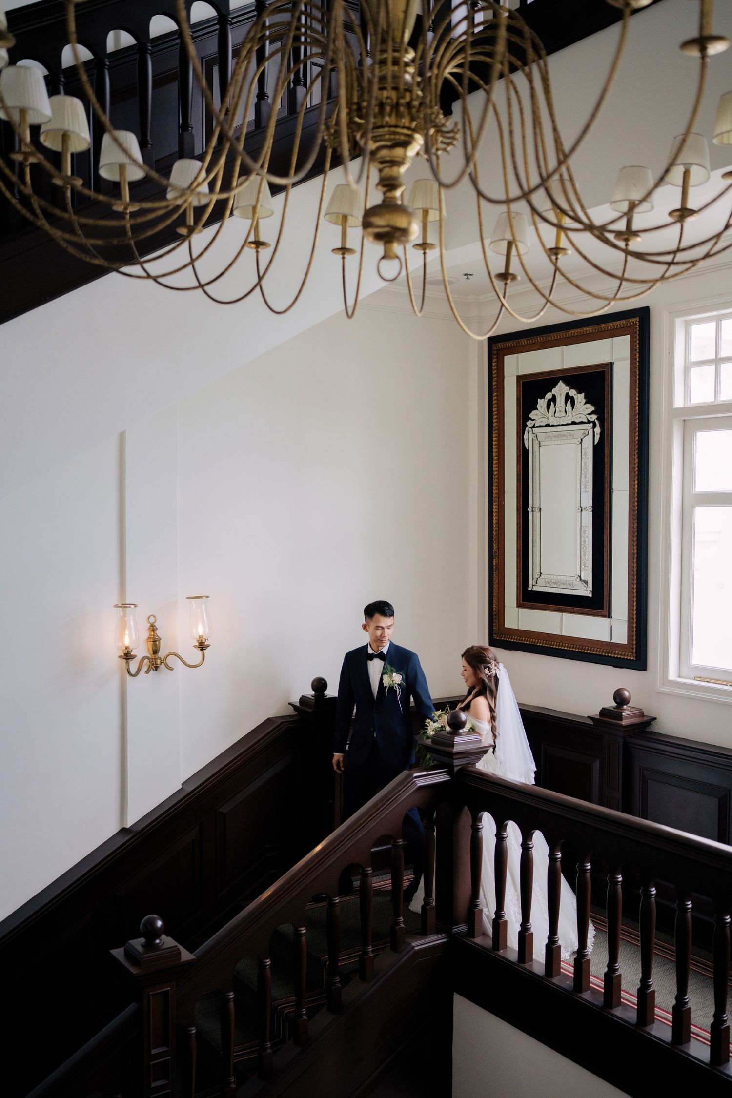 A vintage staircase interior with ornate chandelier and mirror on the wall at Eastern & Oriental Hotel (E&O).