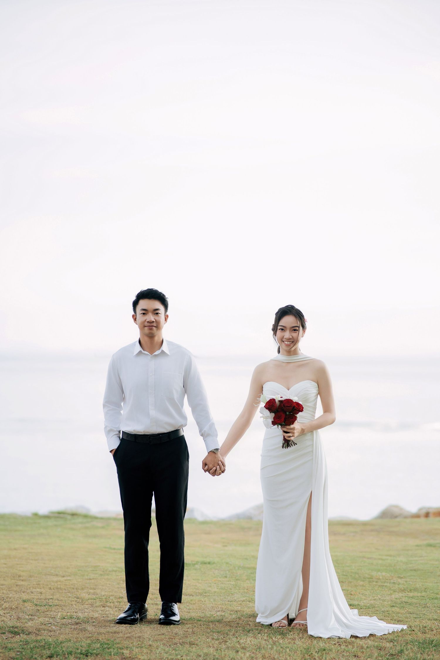 A couple stands together on a grassy hilltop overlooking a scenic landscape.