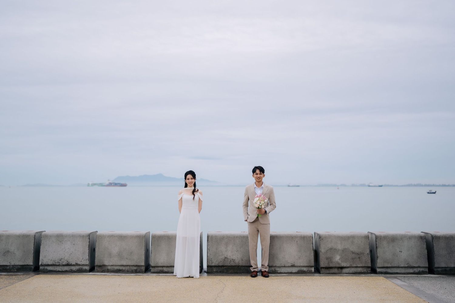 Couple in white attire walking along seaside promenade with misty horizon.